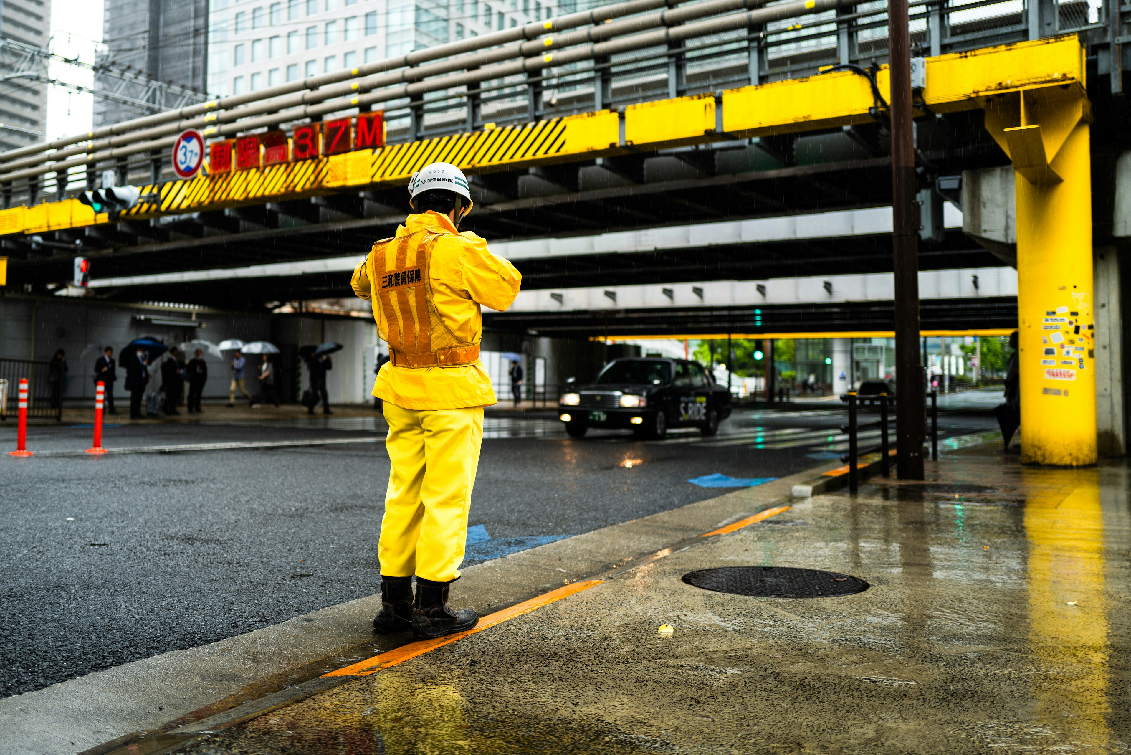 雨の中で黄色いレインコートを着た作業員が立っている街の風景