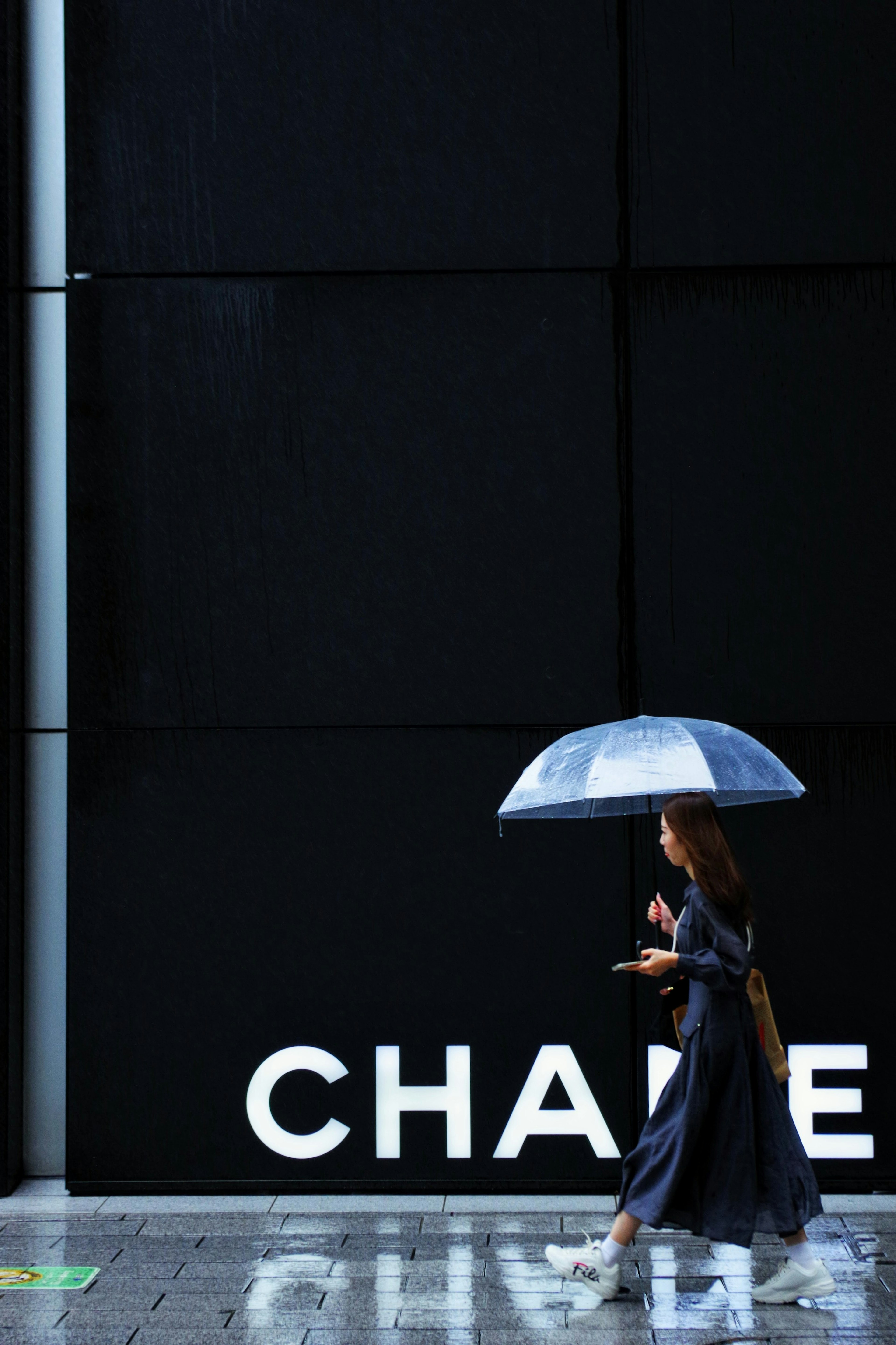 Eine Frau, die mit einem blauen Regenschirm vor einer schwarzen Wand mit dem Wort CHANGE läuft