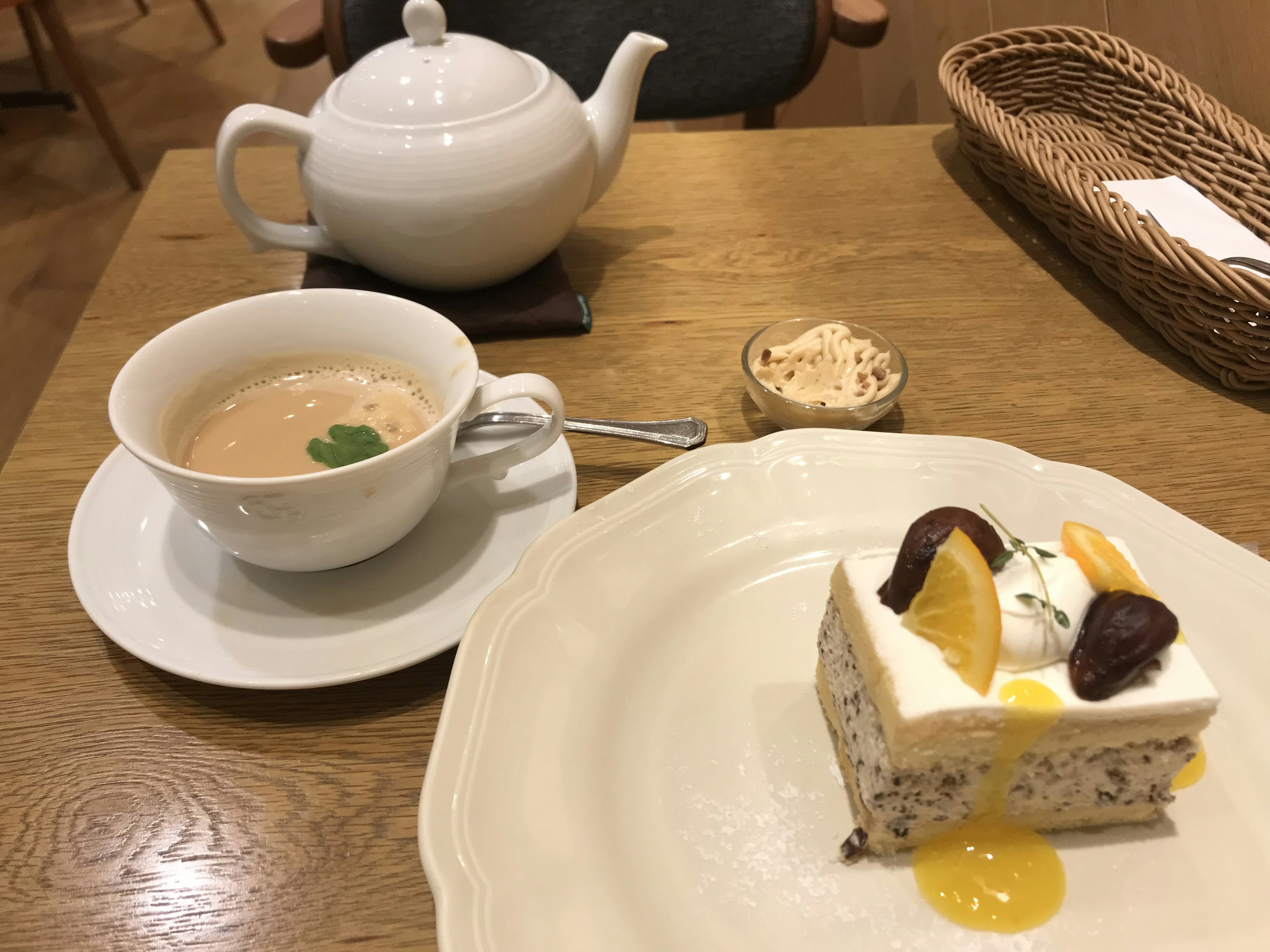 A white teapot and cup of tea with a slice of fruit-topped cake on a cafe table