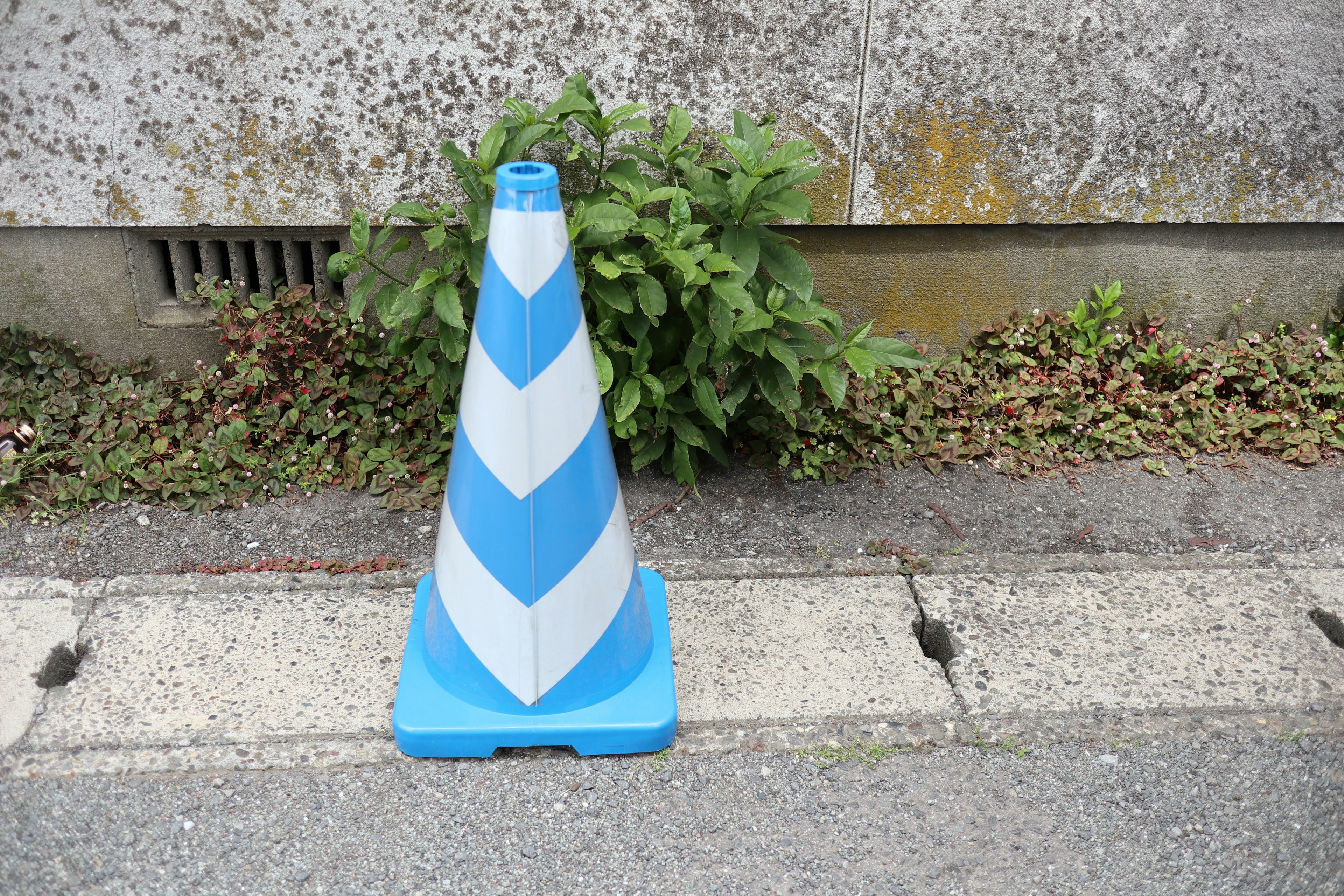 Cono de tráfico azul y blanco de rayas de pie cerca de una pared