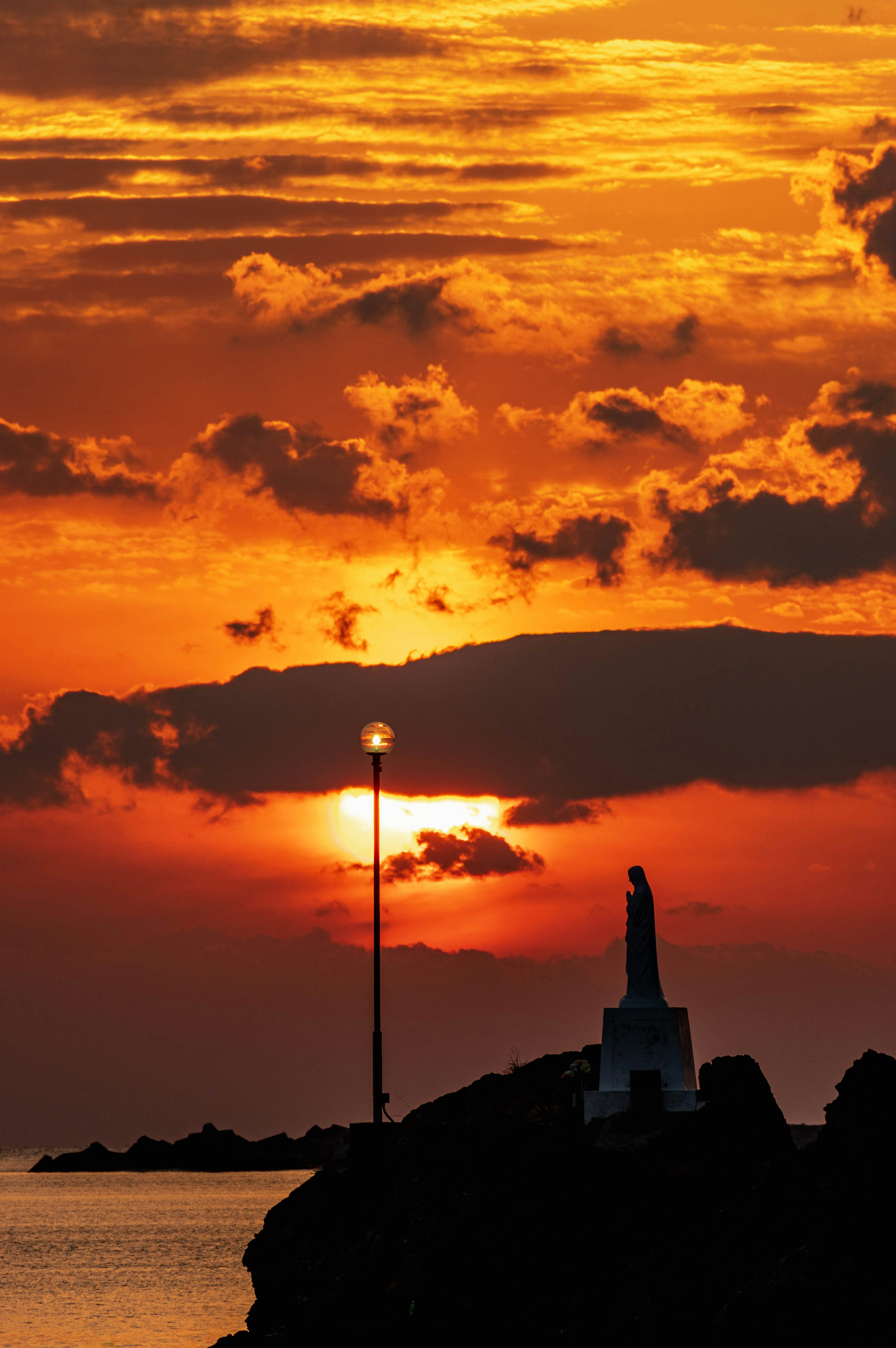 Silhouettierte Statue und Leuchtturm vor einem lebhaften Sonnenuntergangshimmel