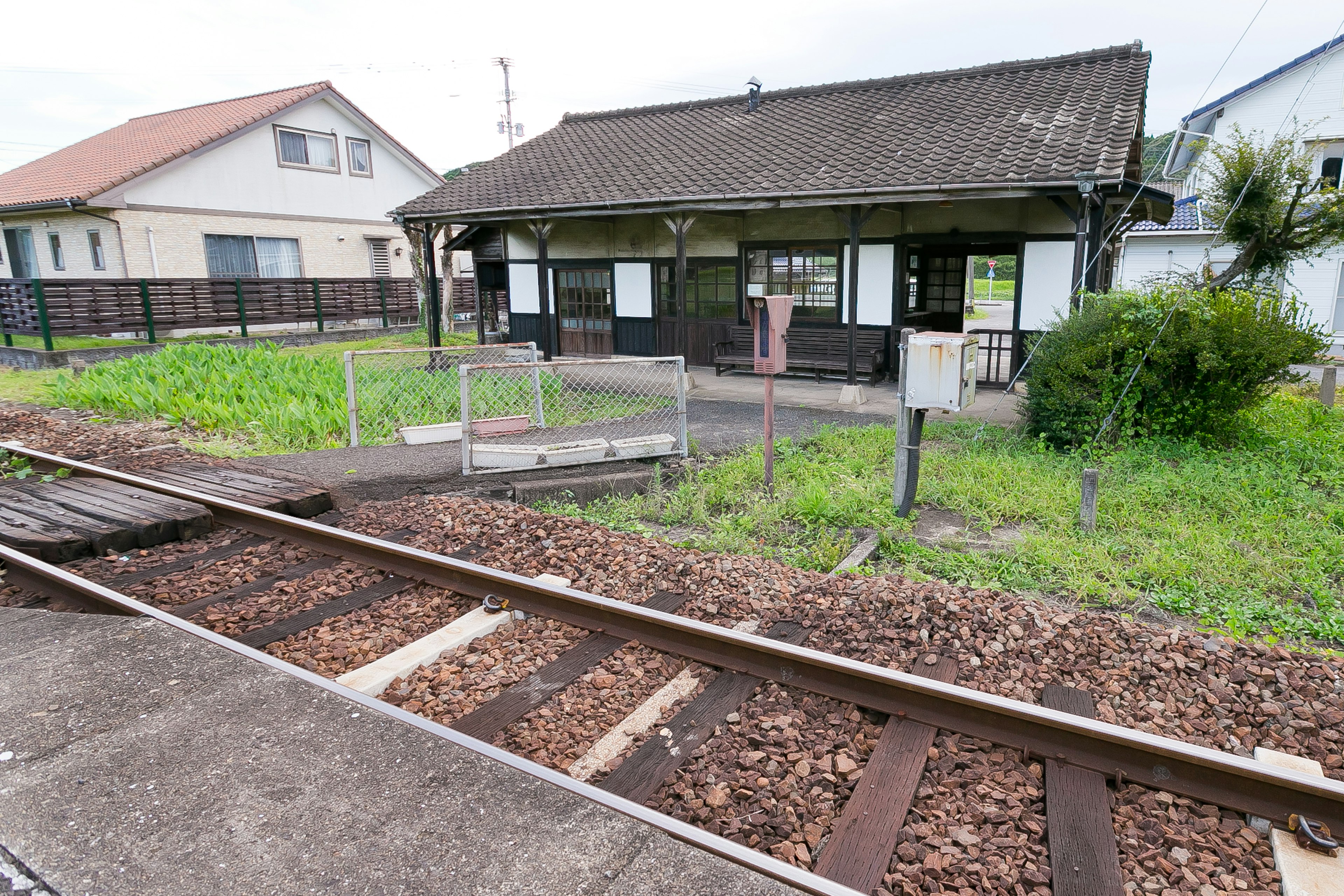 古い駅舎と線路が見える風景 緑の草が生い茂る