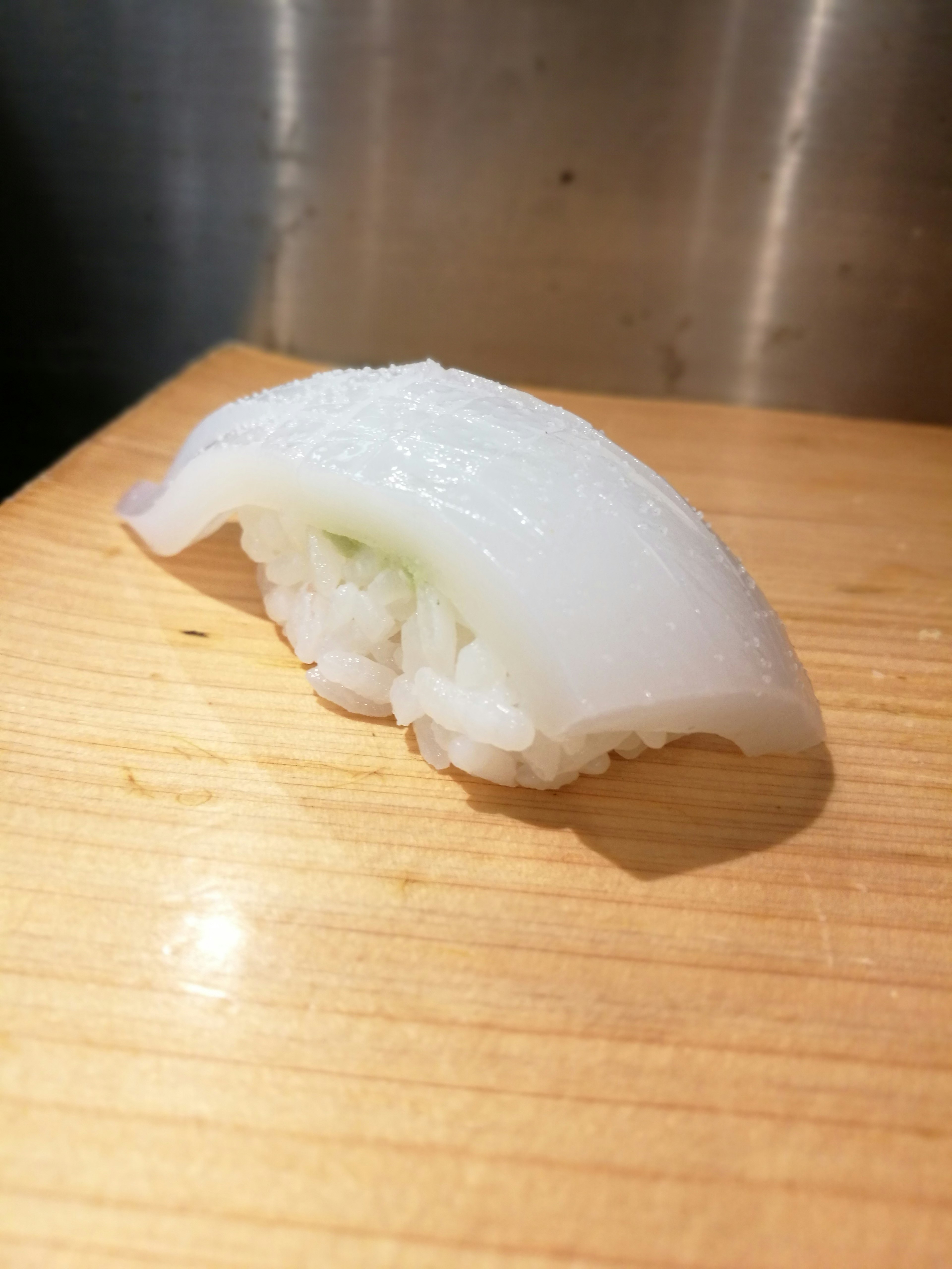 Un nigiri sushi de calmar translucide posé sur une planche en bois