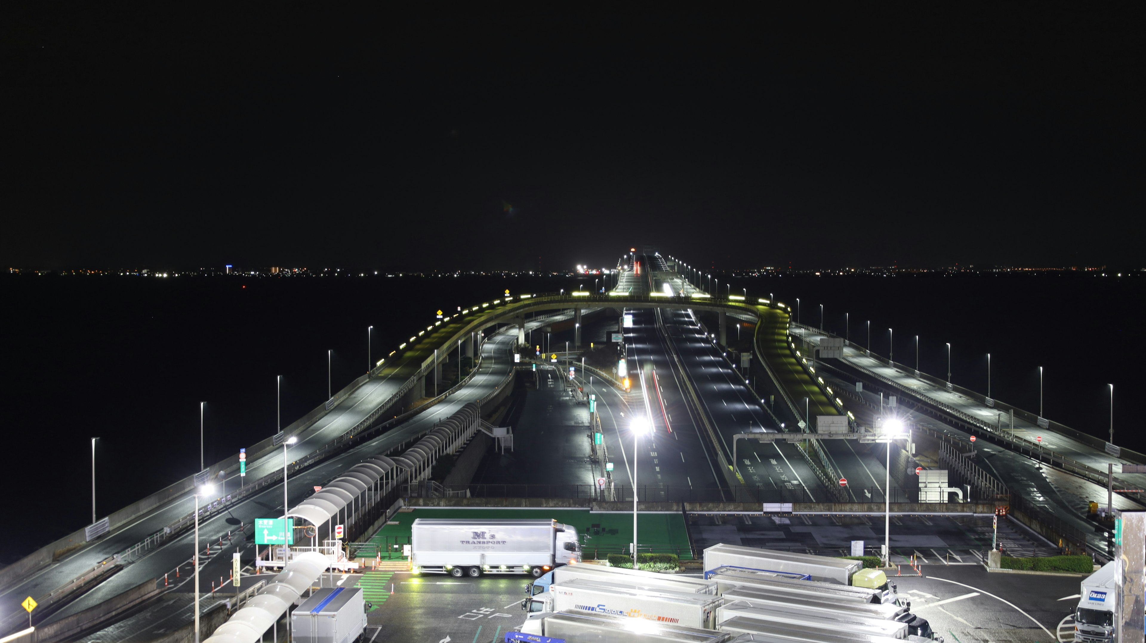 Brightly lit road and lined trucks at a port at night