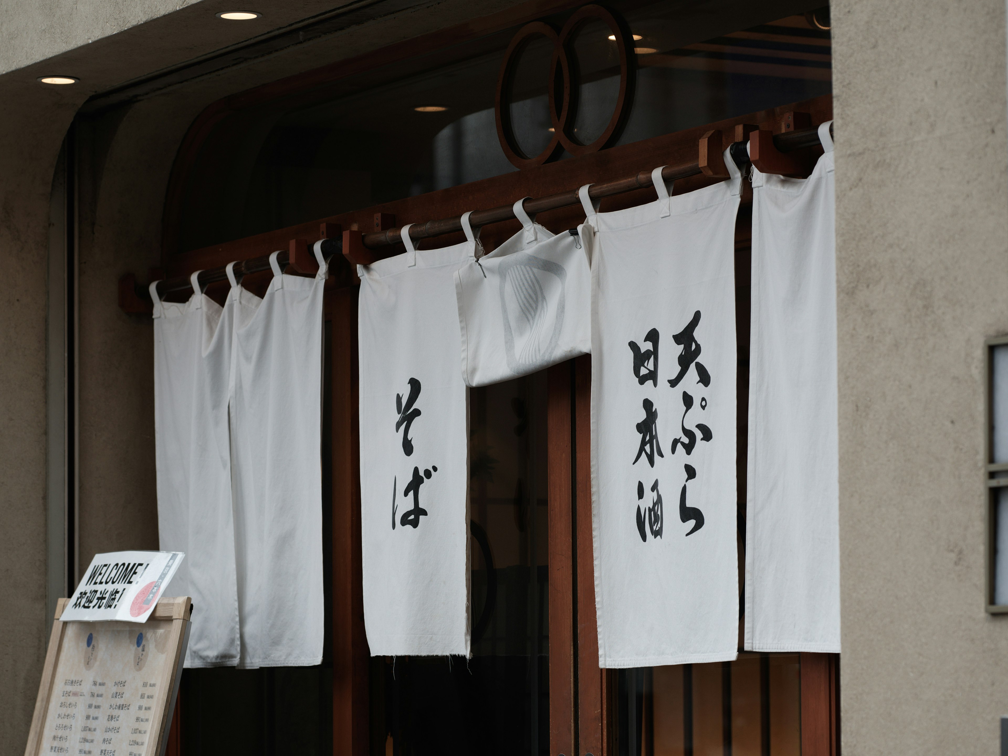 Entrada de un restaurante de soba con un noren blanco que muestra caligrafía japonesa