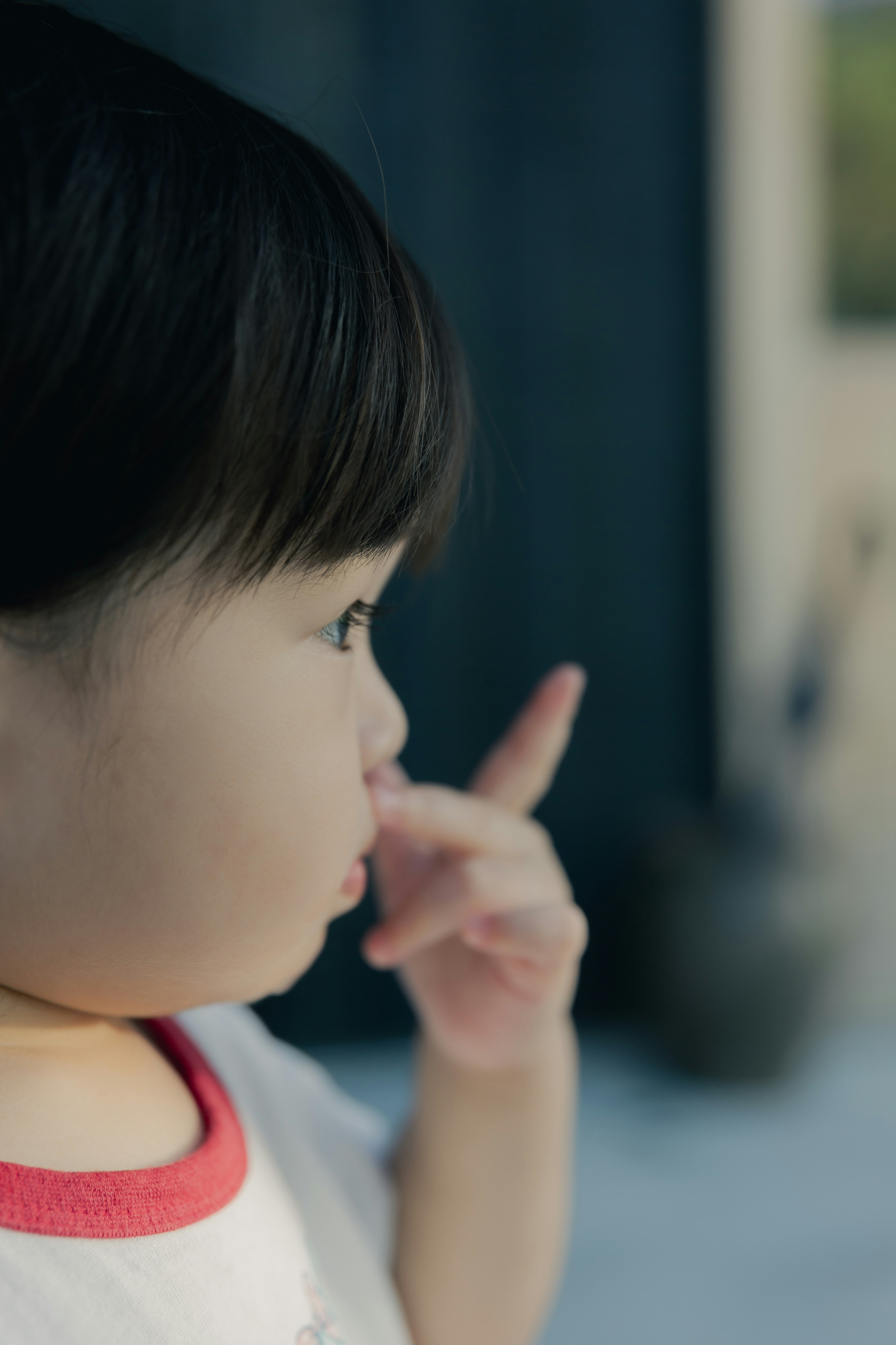 Un bambino in una maglietta con bordo rosso alza un dito di profilo