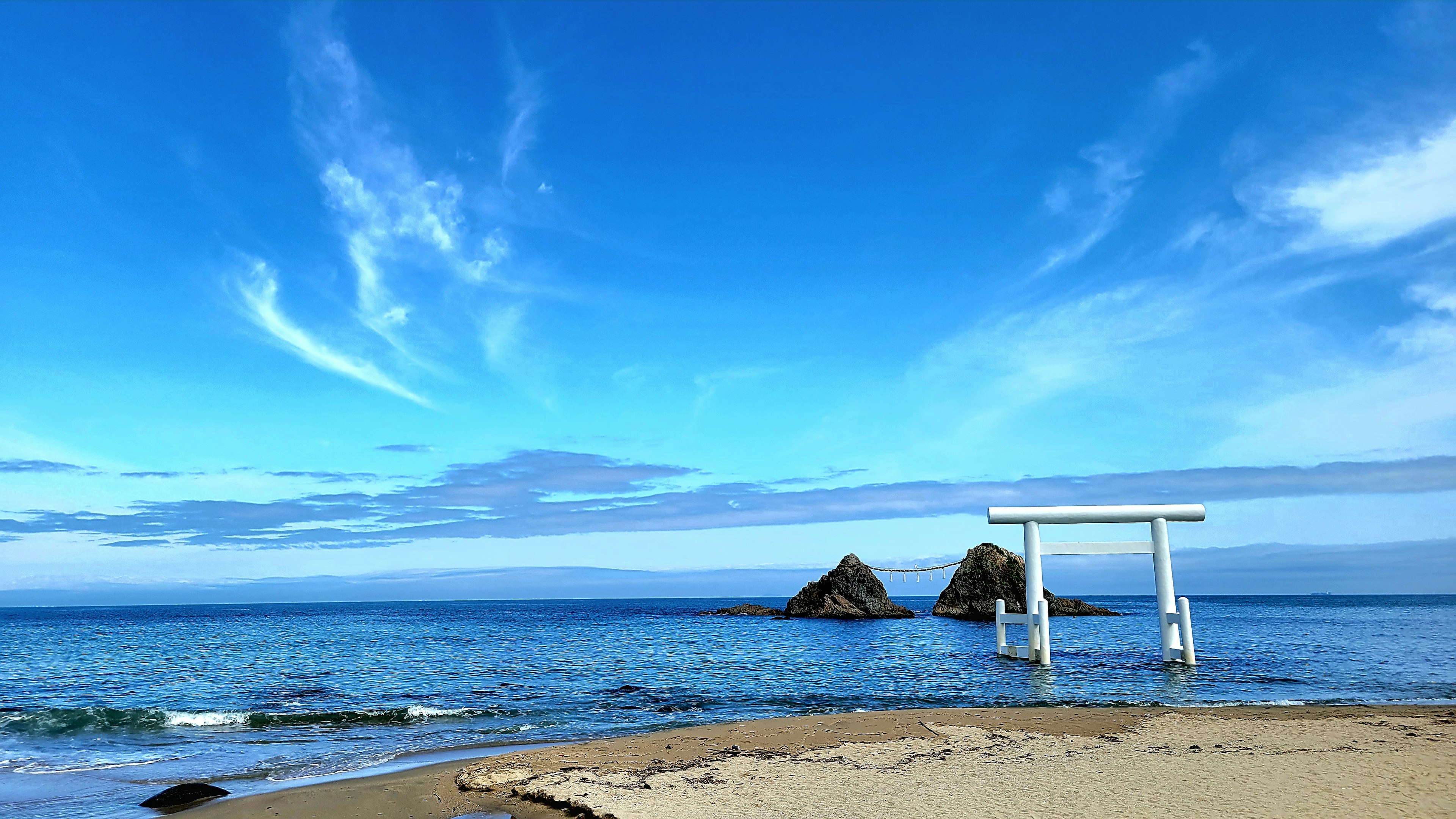 Escena de playa con un torii y formaciones rocosas bajo un cielo azul