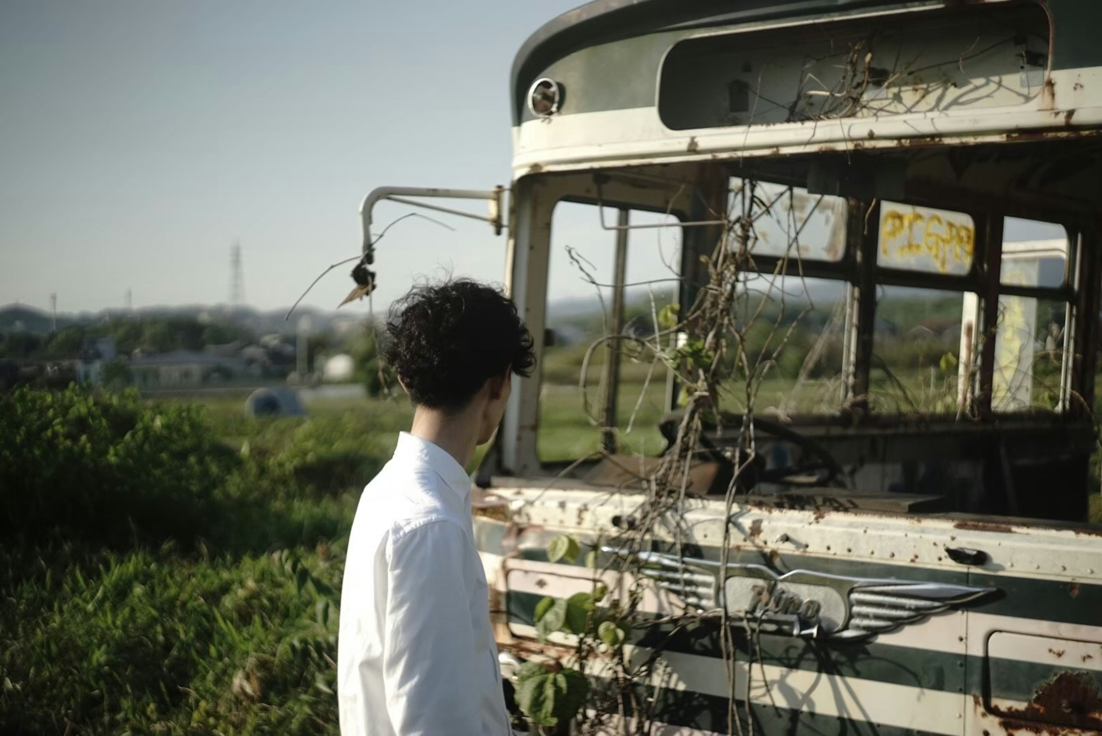 廃車のバスと若い男性の姿が映る風景の写真