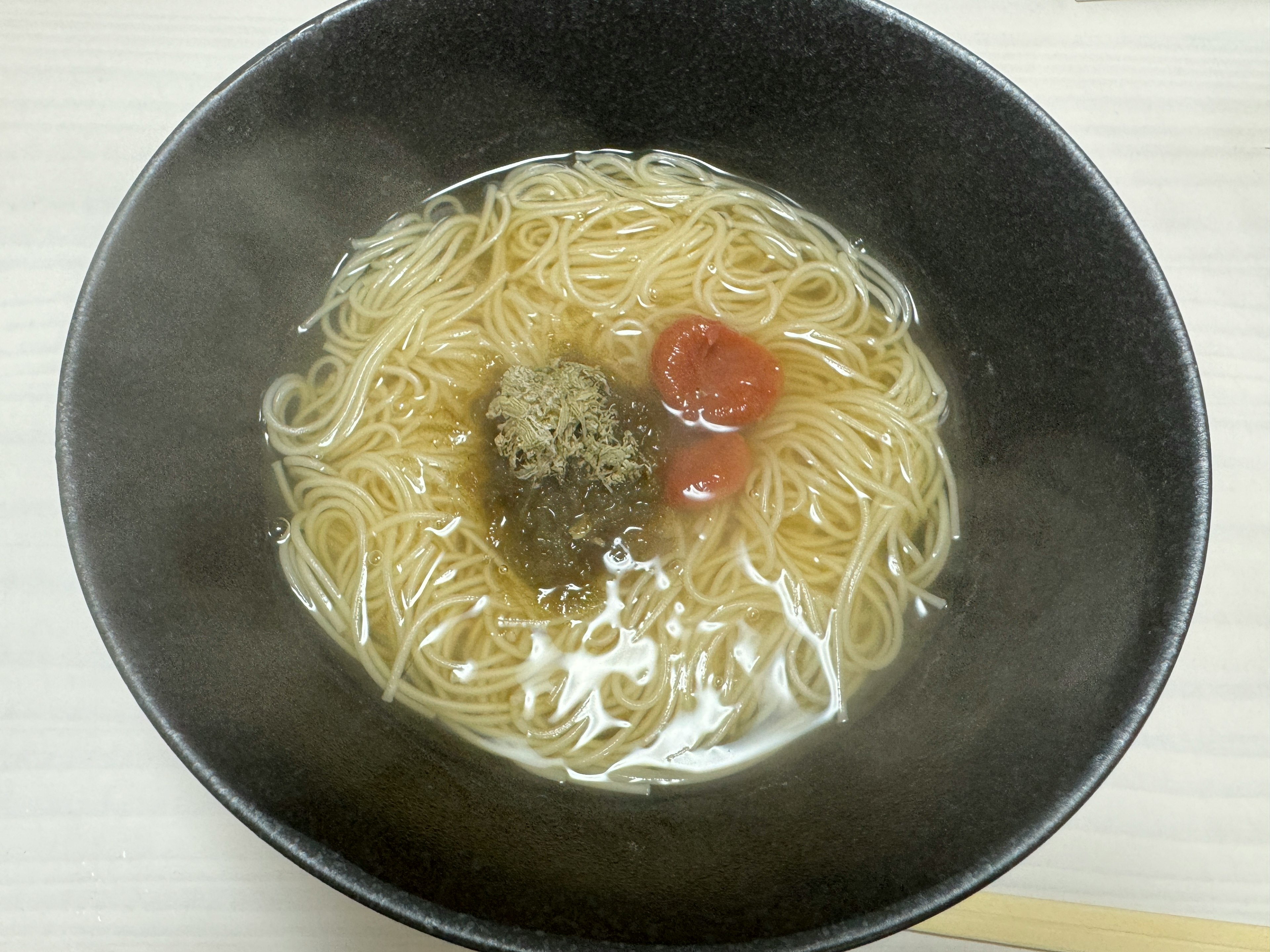 熱々のラーメンが入った黒いボウルに細麺とトッピングの梅干しと海苔