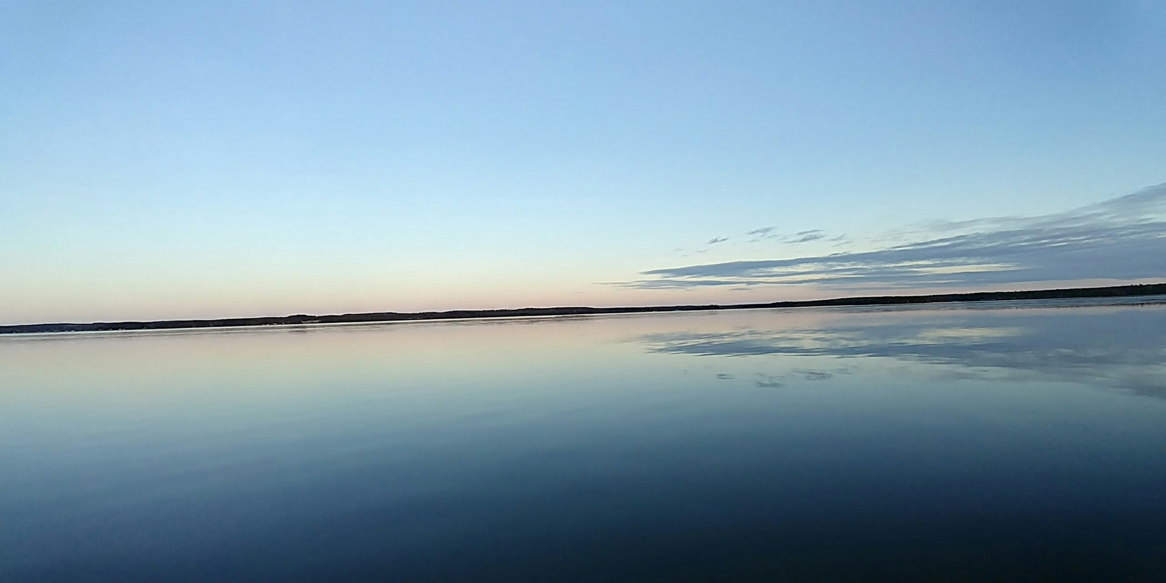 Ruhige Wasseroberfläche, die einen klaren blauen Himmel spiegelt