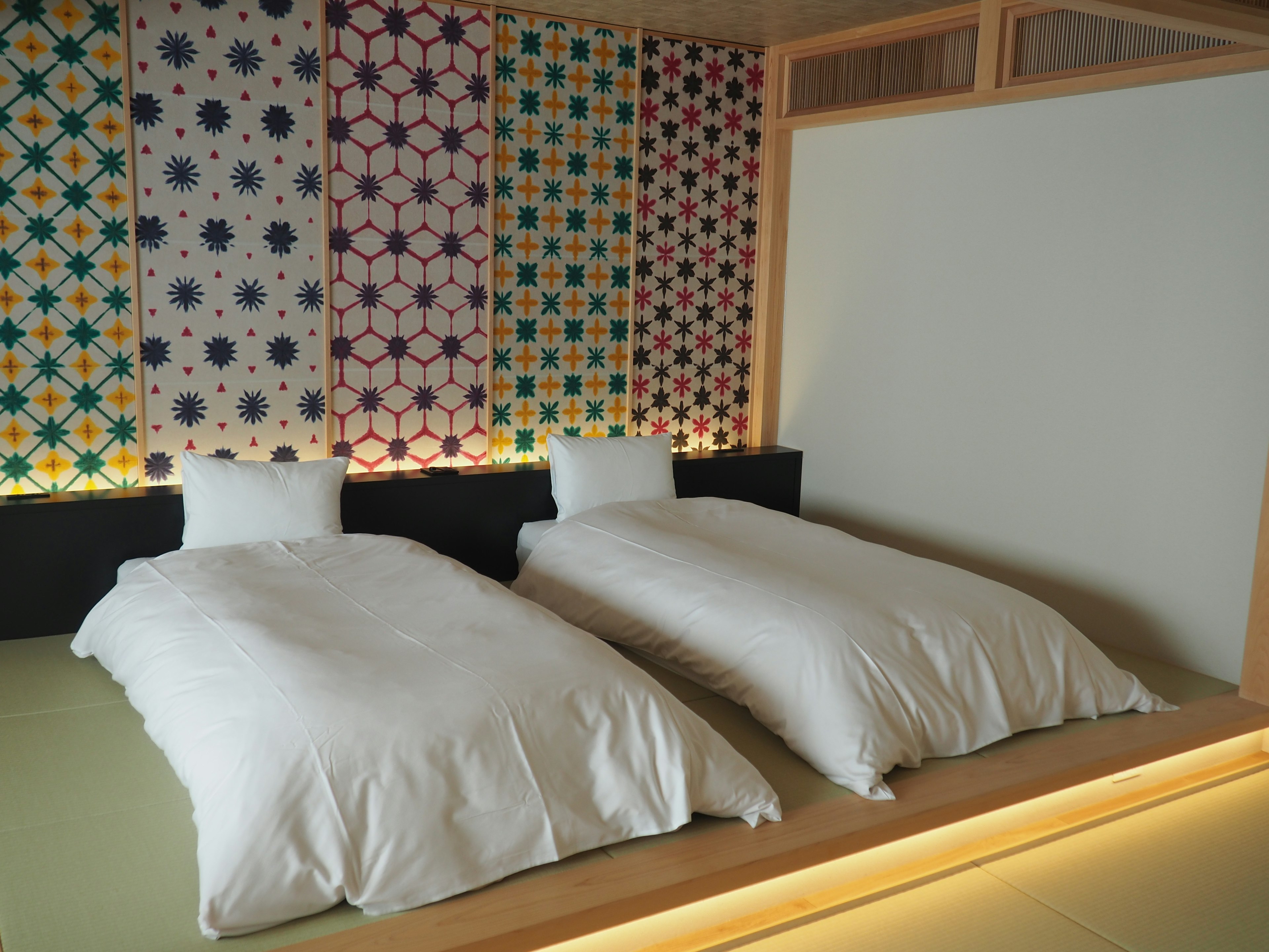 Une chambre avec deux futons blancs et un mur à motifs colorés