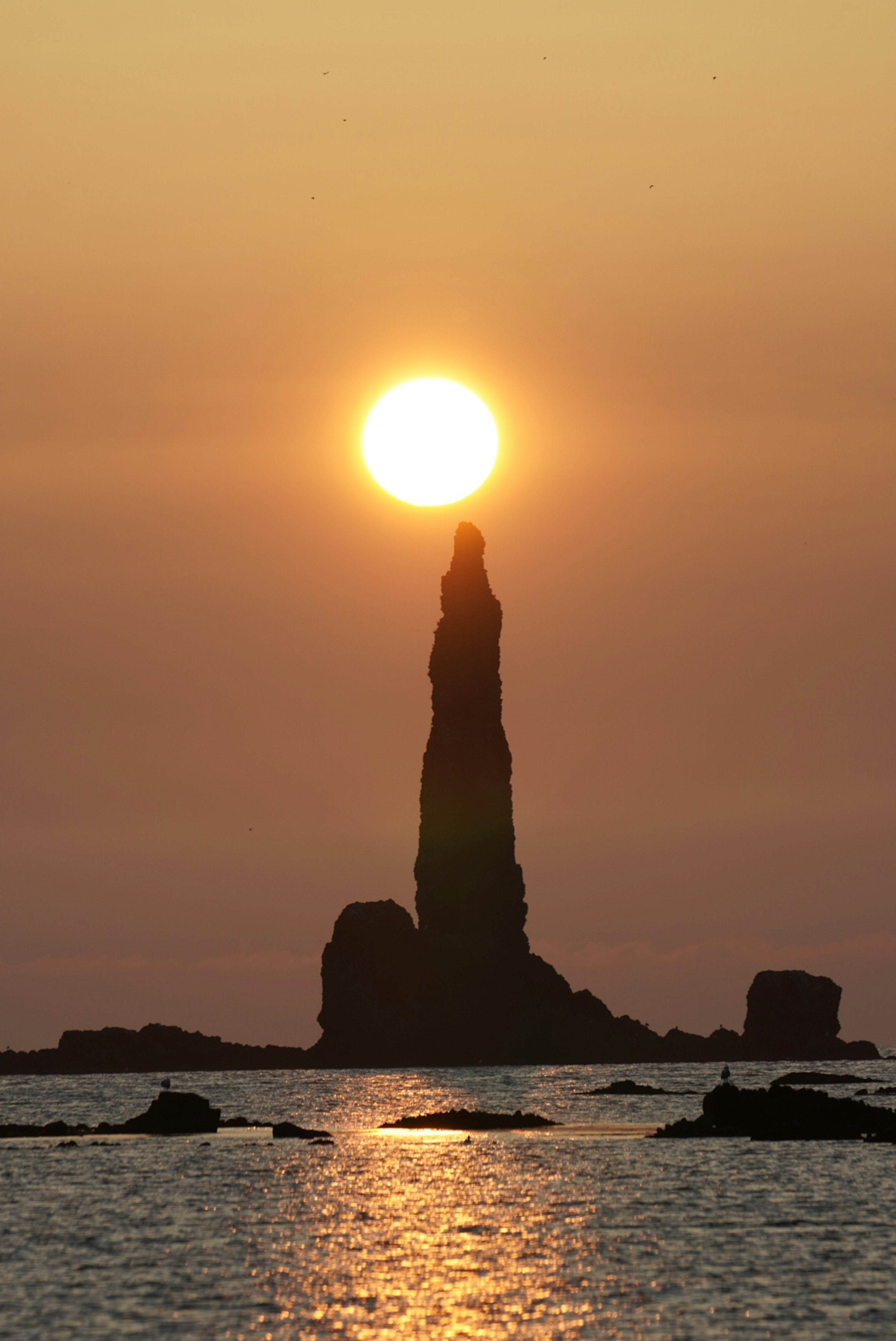 Beautiful seascape with the sun setting behind a jagged rock formation