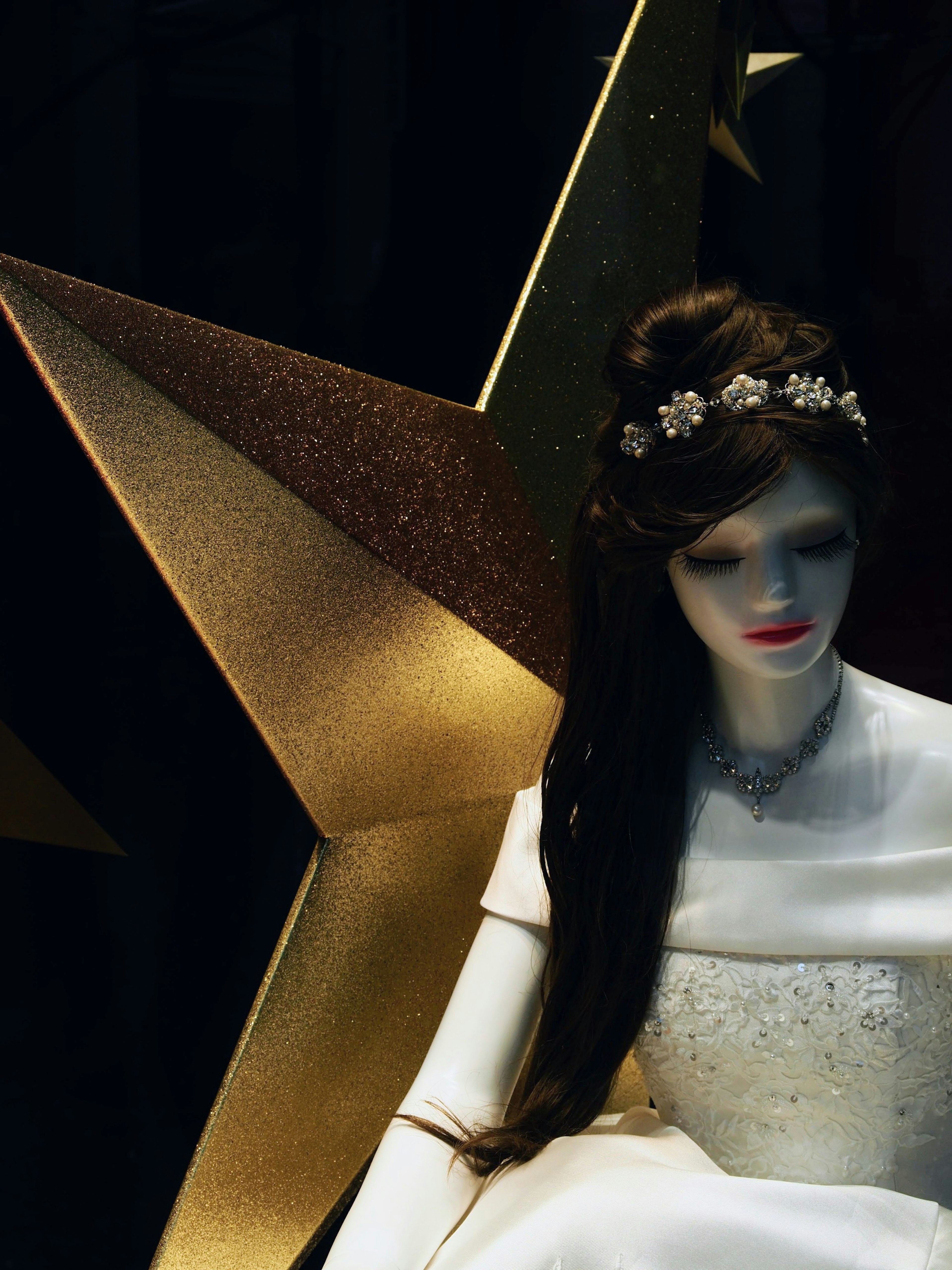 A mannequin dressed in a white gown sitting against a golden star background