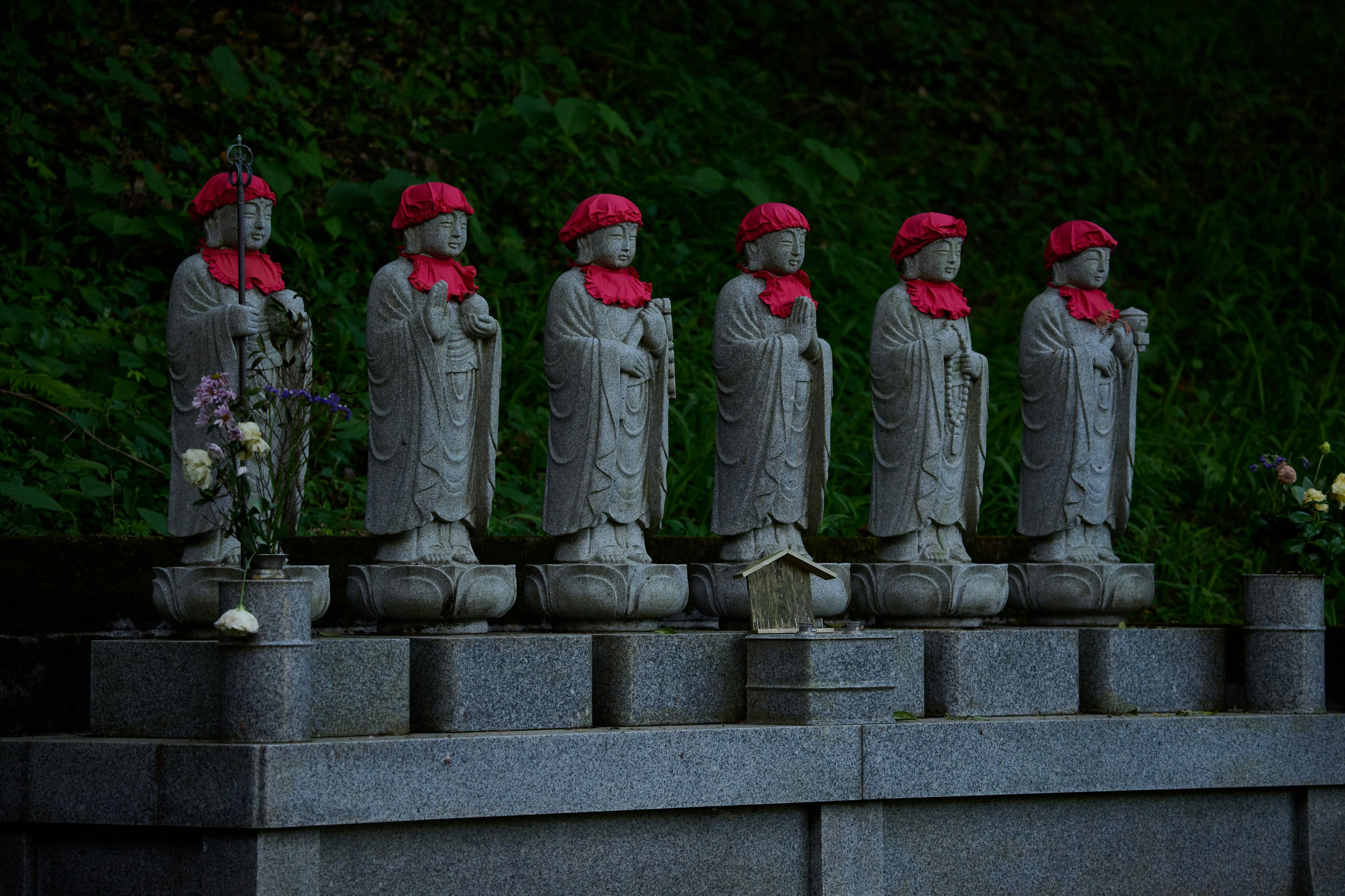 Six statues en pierre portant des chapeaux rouges disposées dans un cadre serein