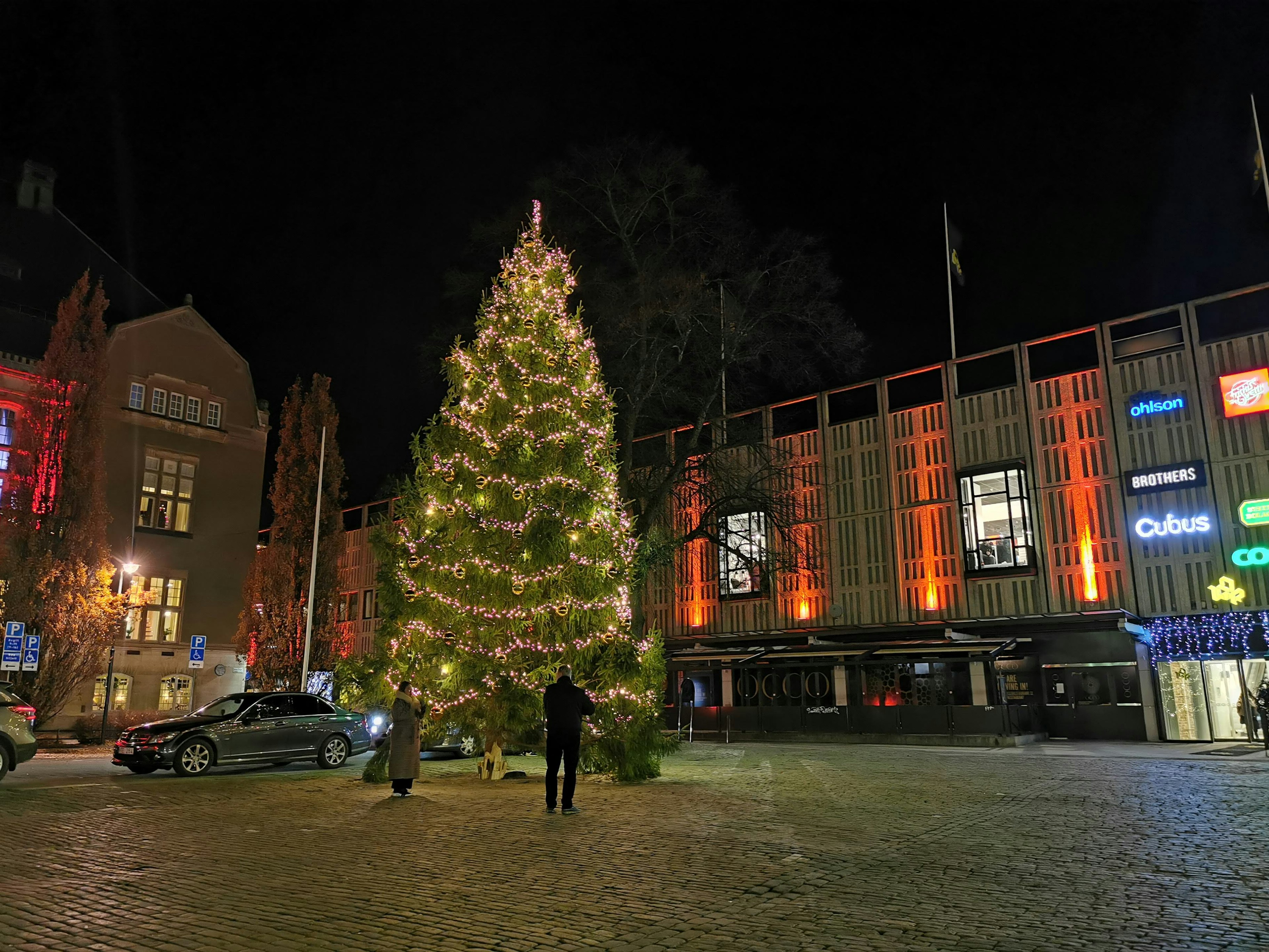 Grand arbre de Noël illuminé la nuit dans une place publique avec des bâtiments environnants