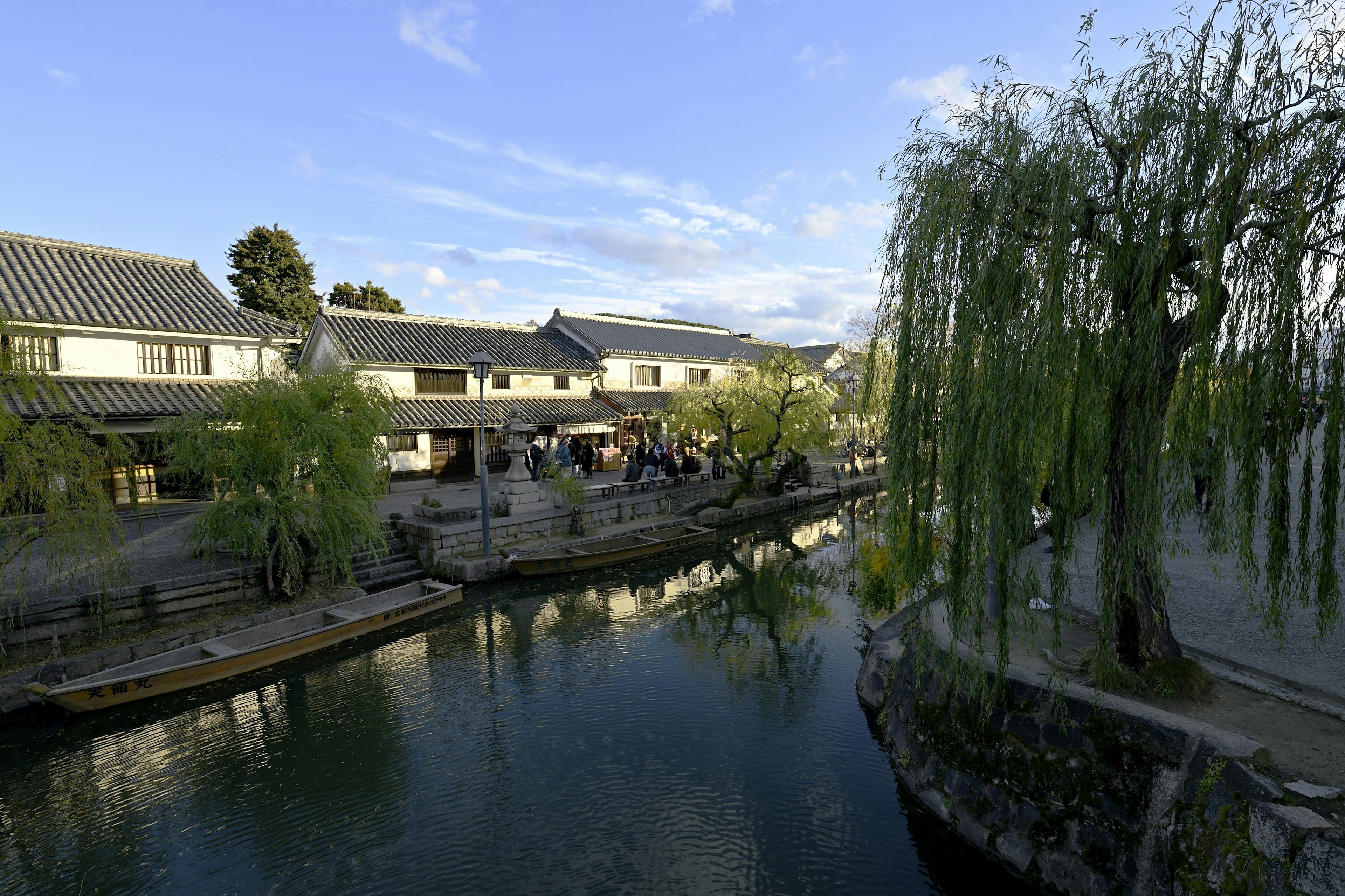 Scenic riverside view featuring willow trees and traditional buildings