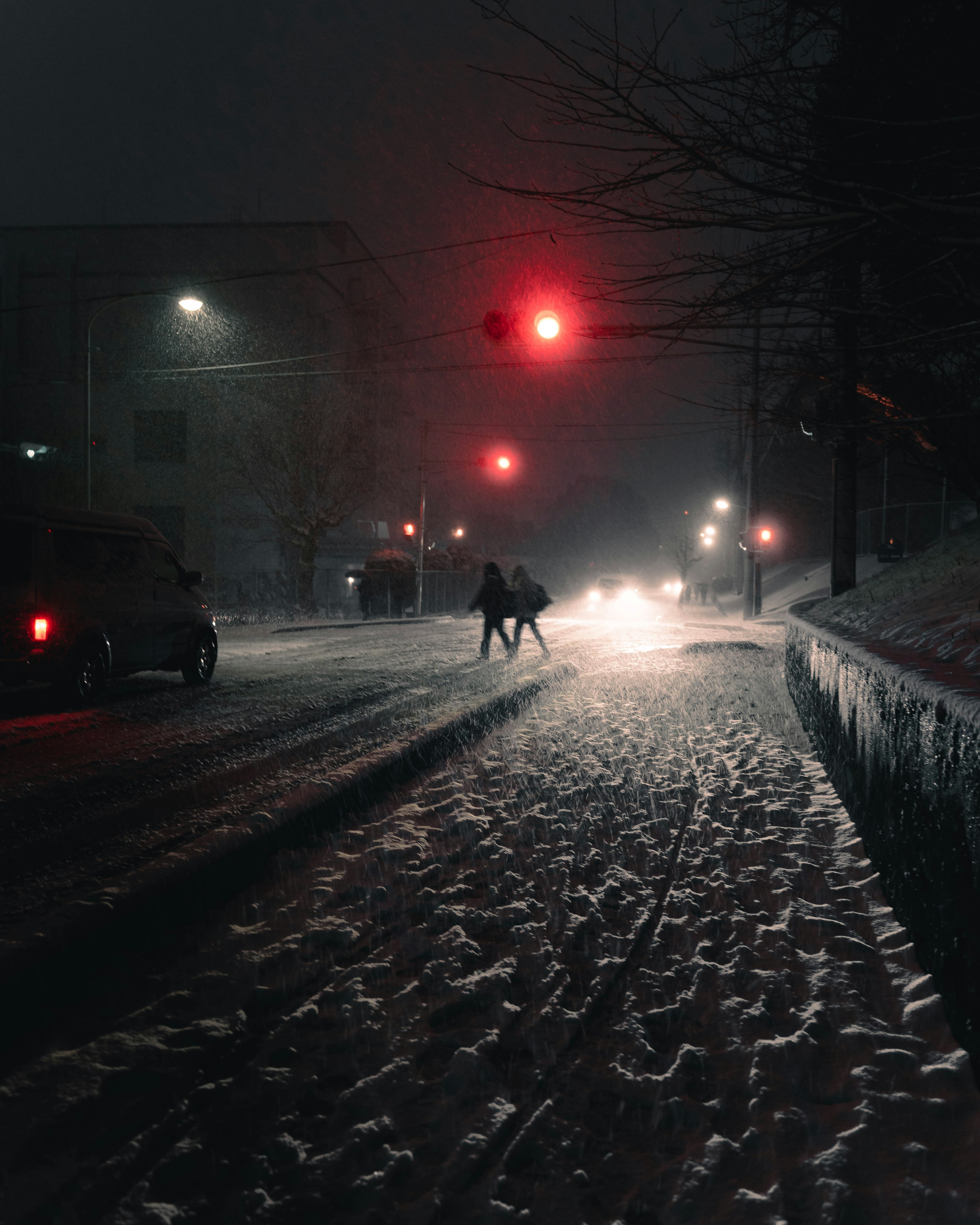 People walking in a snowy street at night with a red traffic light