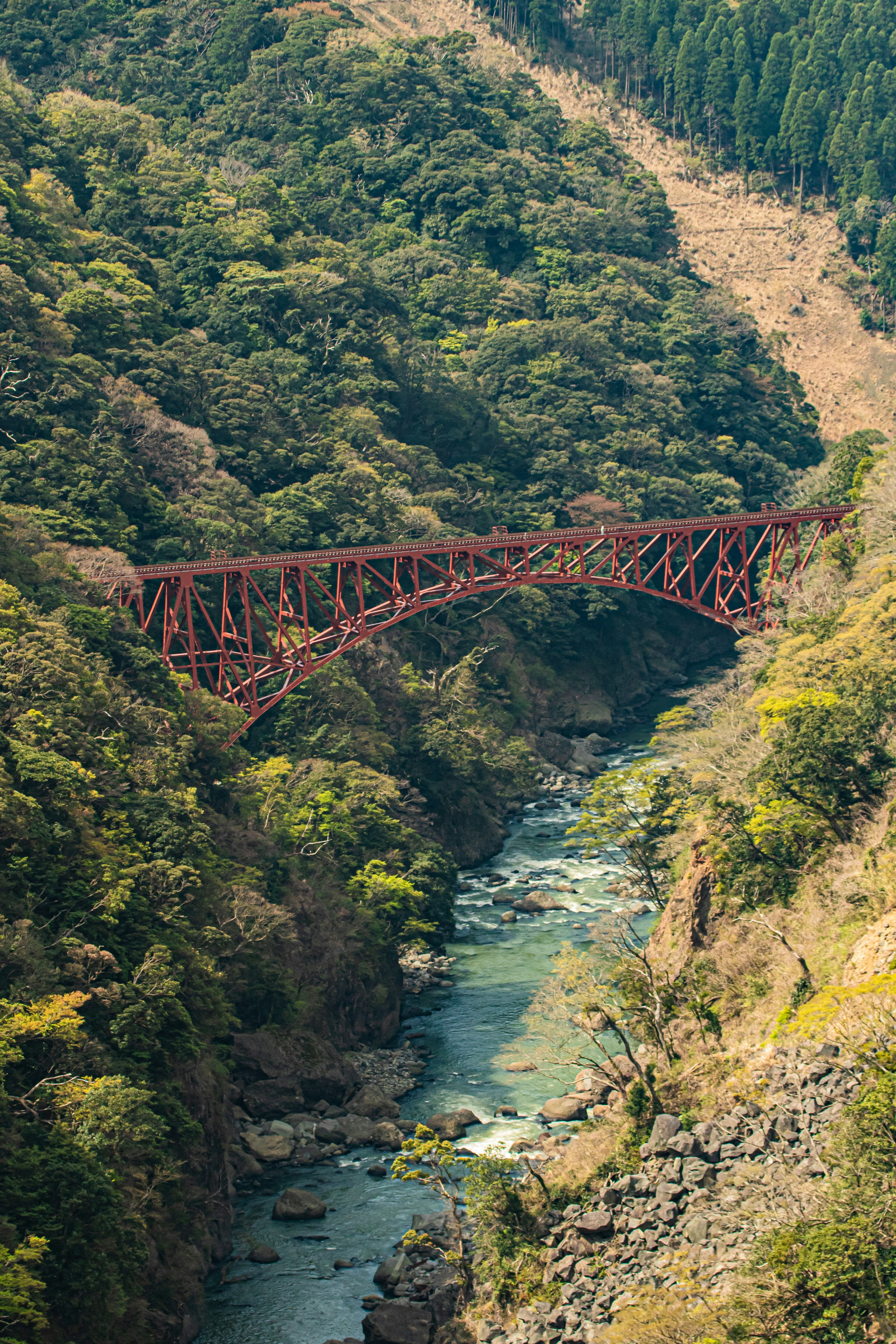 Red iron bridge spanning a lush green valley with a river