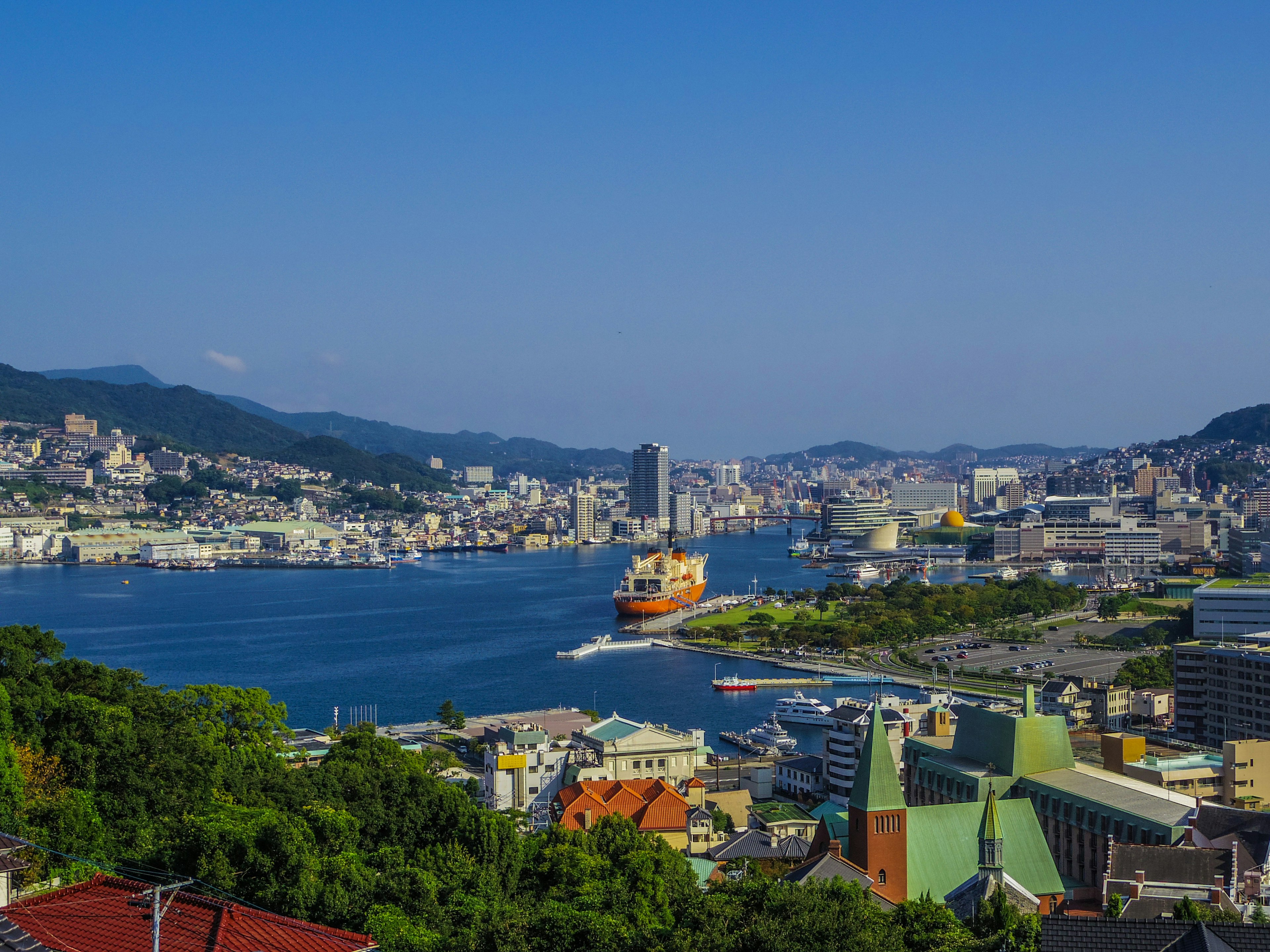 ทิวทัศน์ของท่าเรือนากาซากิกับเส้นขอบฟ้าของเมืองและภูเขาในพื้นหลัง