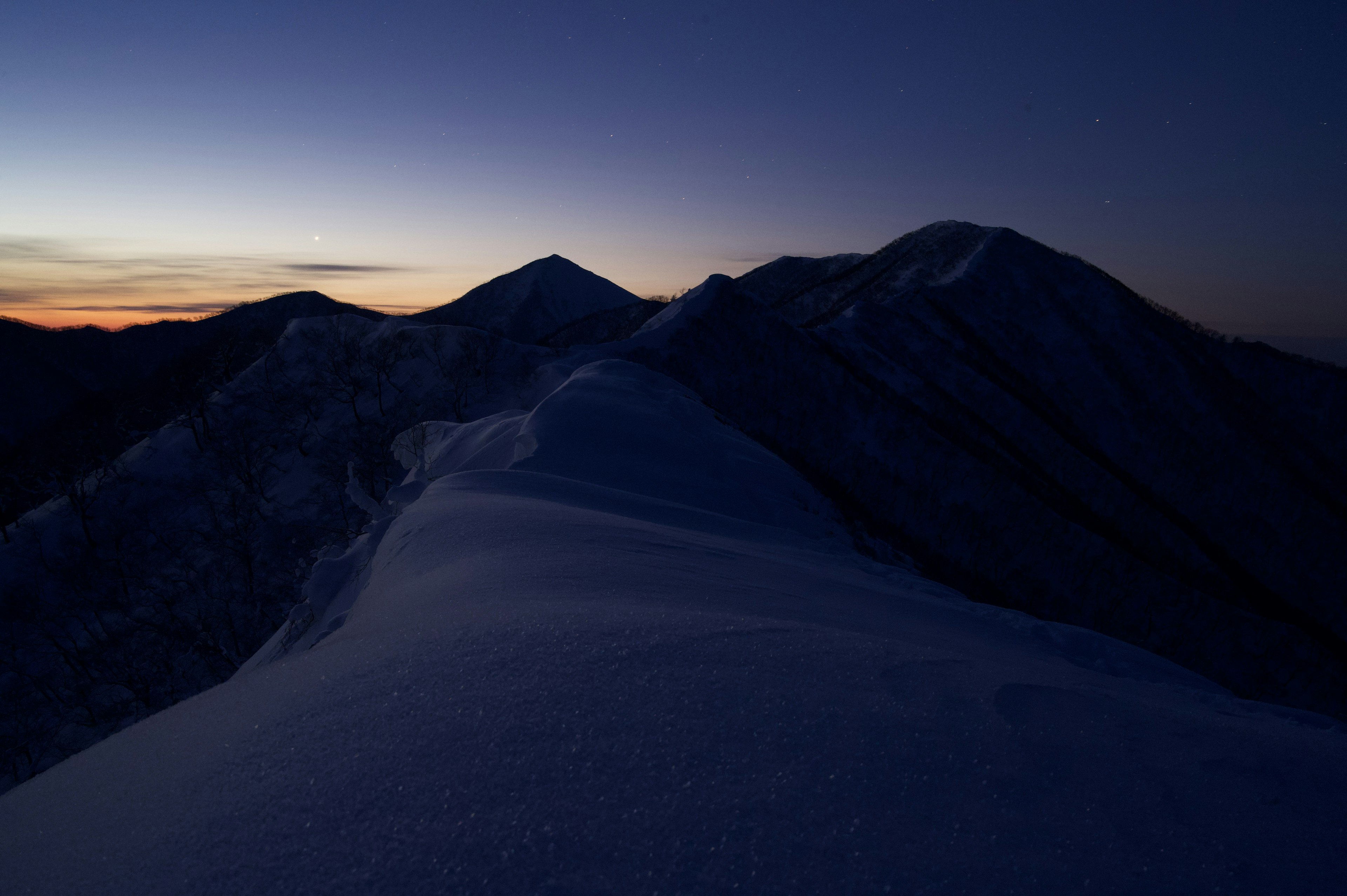 Cresta di montagna coperta di neve sotto un cielo crepuscolare