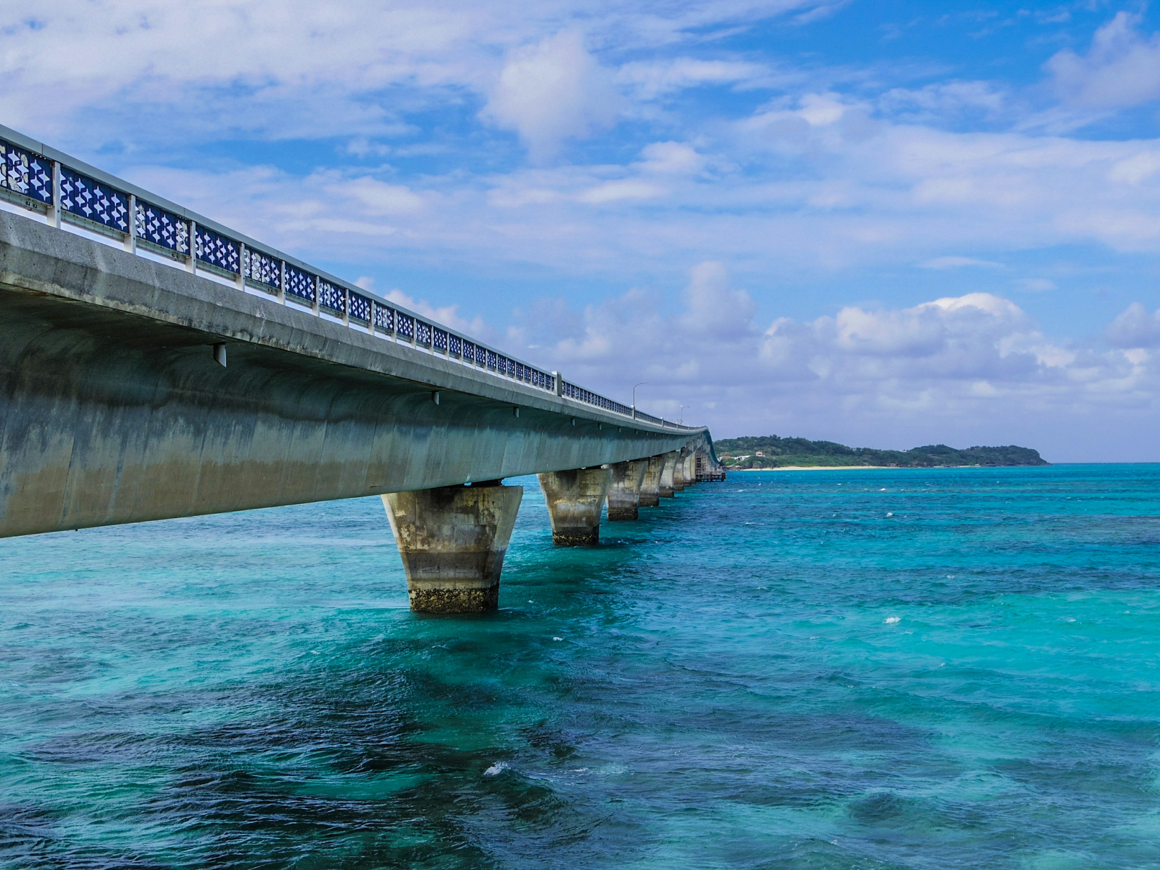 Sebuah jembatan yang membentang di atas lautan biru dengan gelombang yang terlihat di bawah