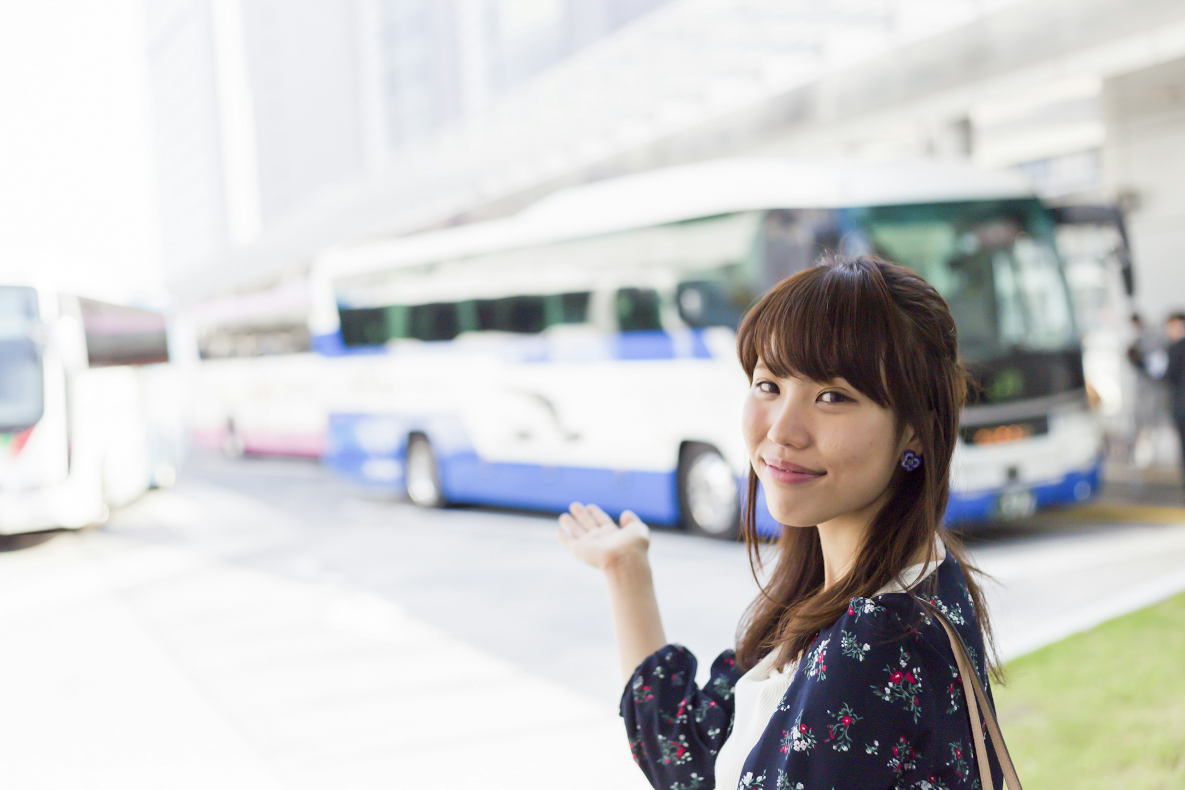 A woman waving at a bus stop with buses parked in the background