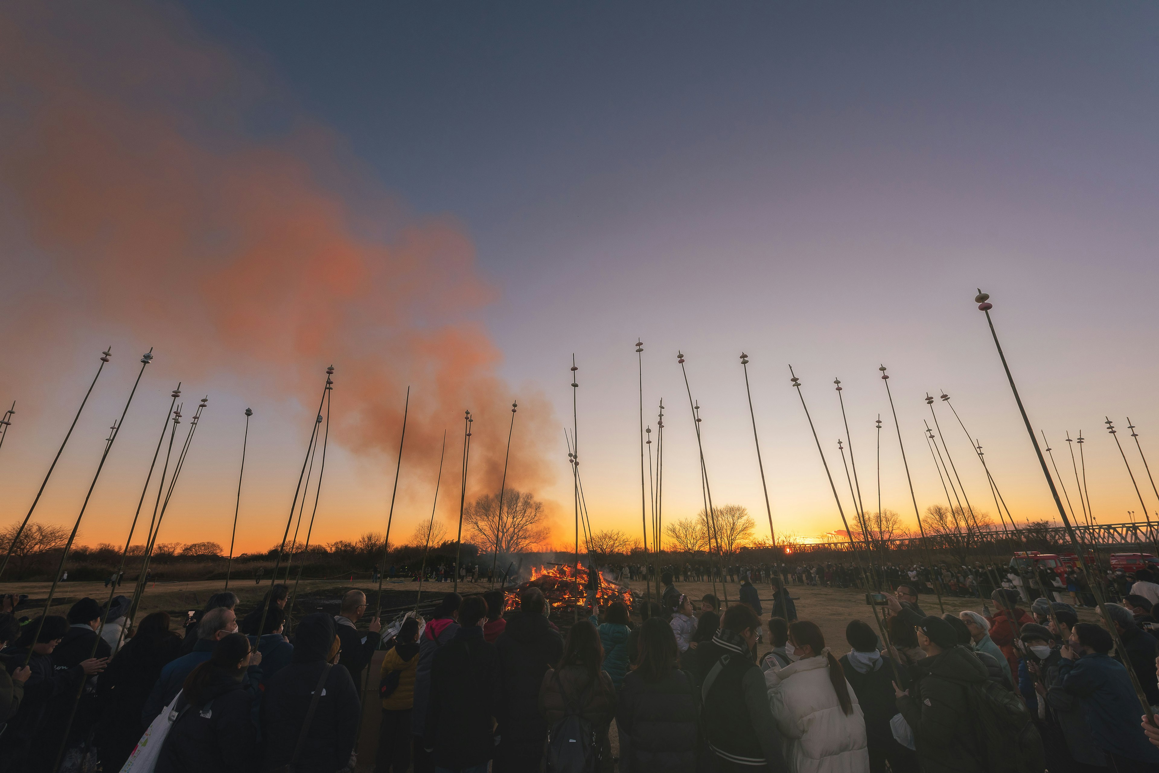 Crowd watching smoke rising at sunset with silhouetted poles