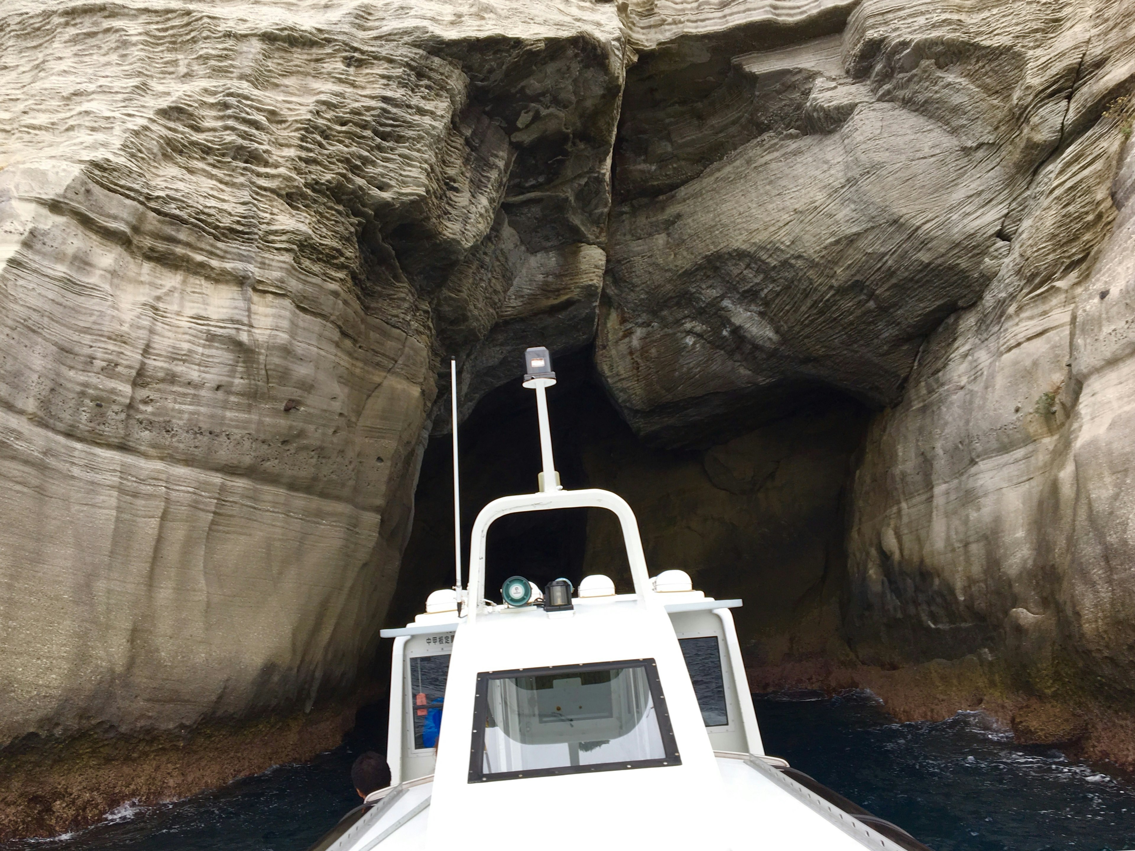 Barca bianca che si avvicina all'ingresso di una grotta circondata da scogliere rocciose