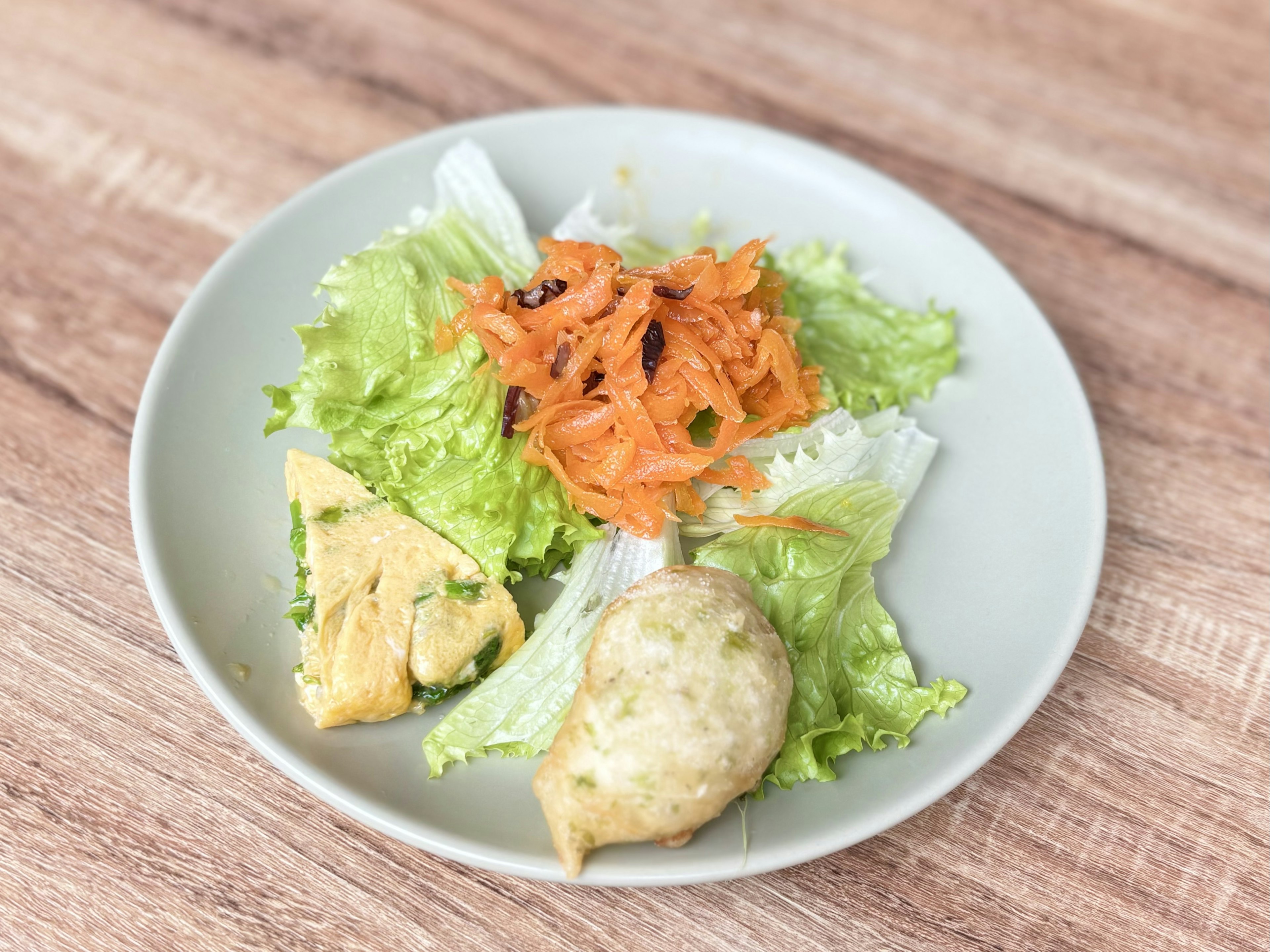 Piring dengan selada hijau dan salad wortel, dilengkapi dengan omelet dan makanan goreng