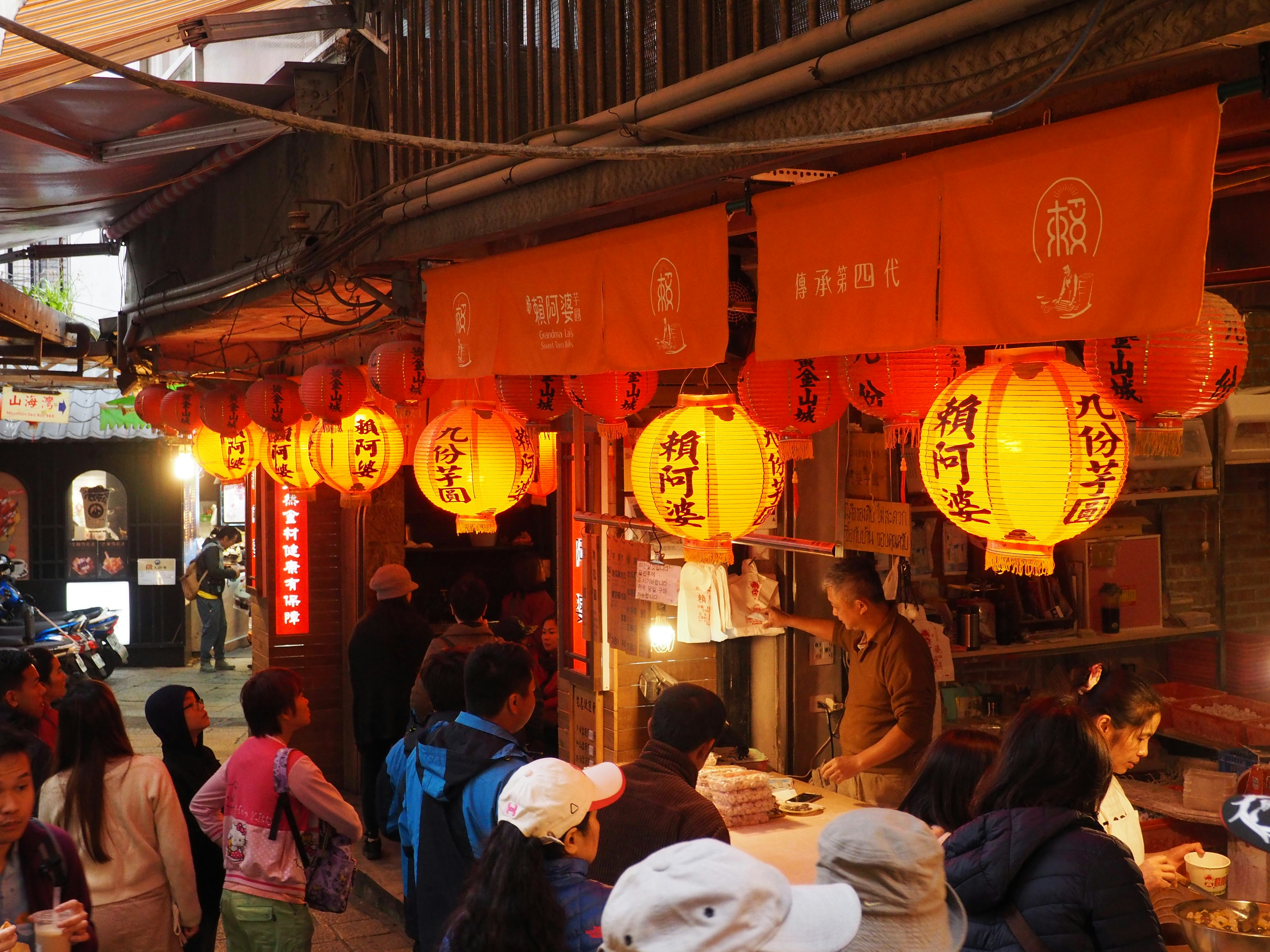 Busy night market stall with orange lanterns and people in line