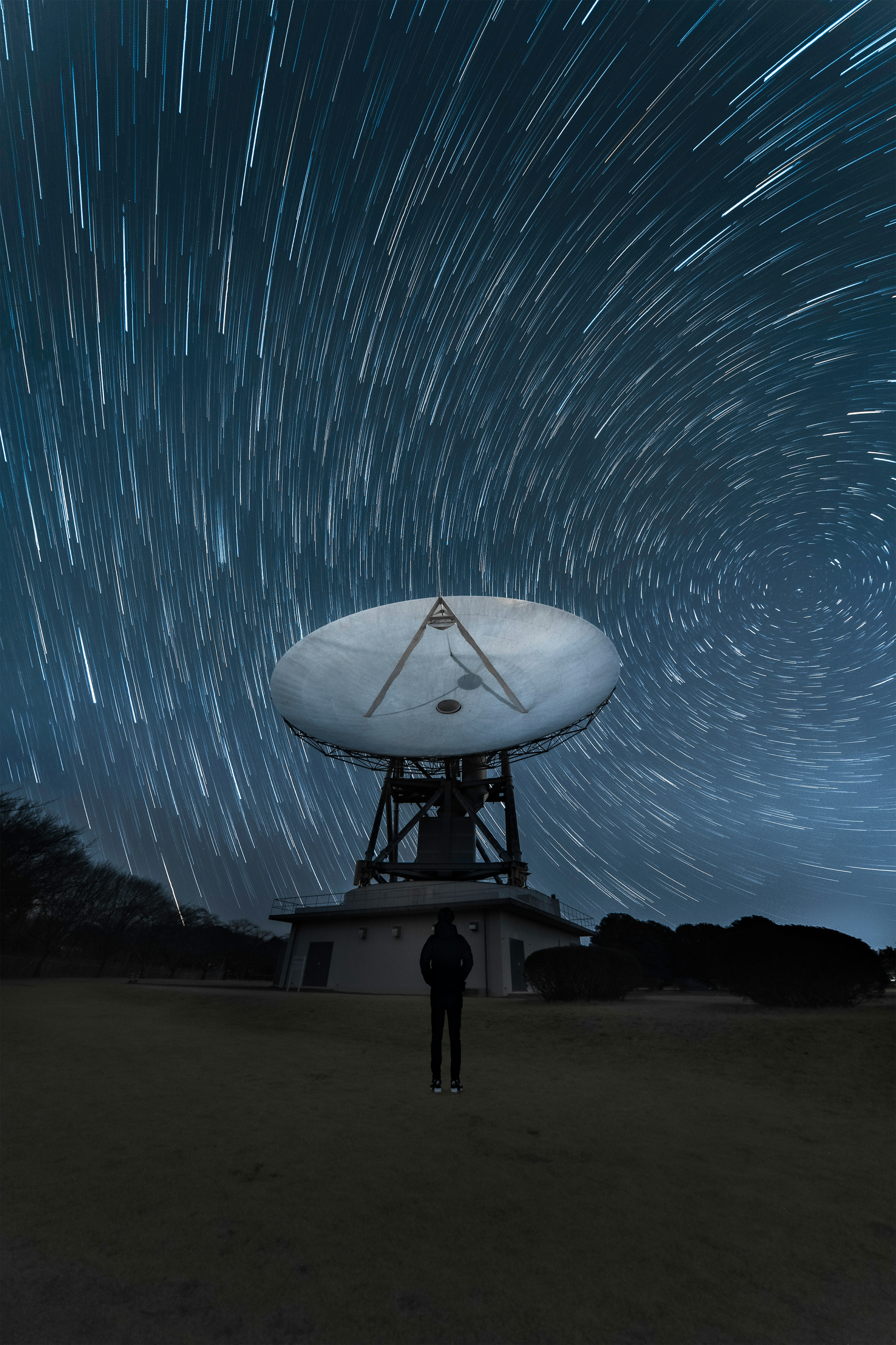 Imagen de una persona de pie bajo las estelas de estrellas con una gran antena parabólica