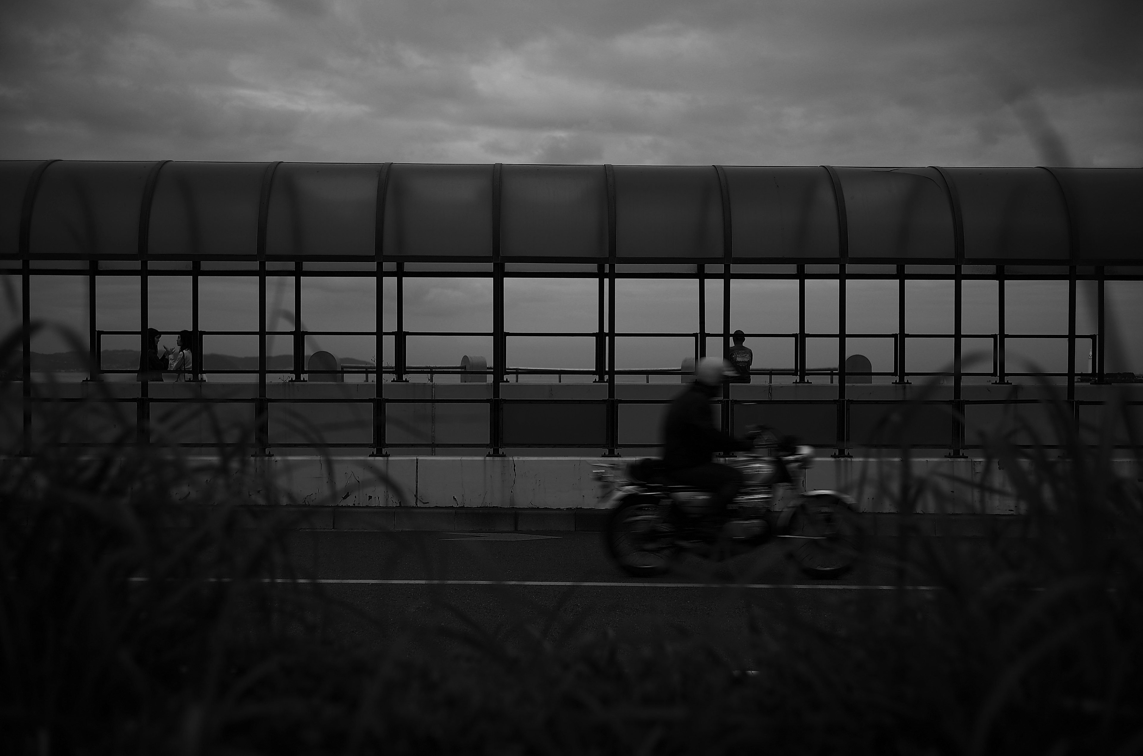 Une personne à moto passant devant une structure en verre dans un paysage monochrome