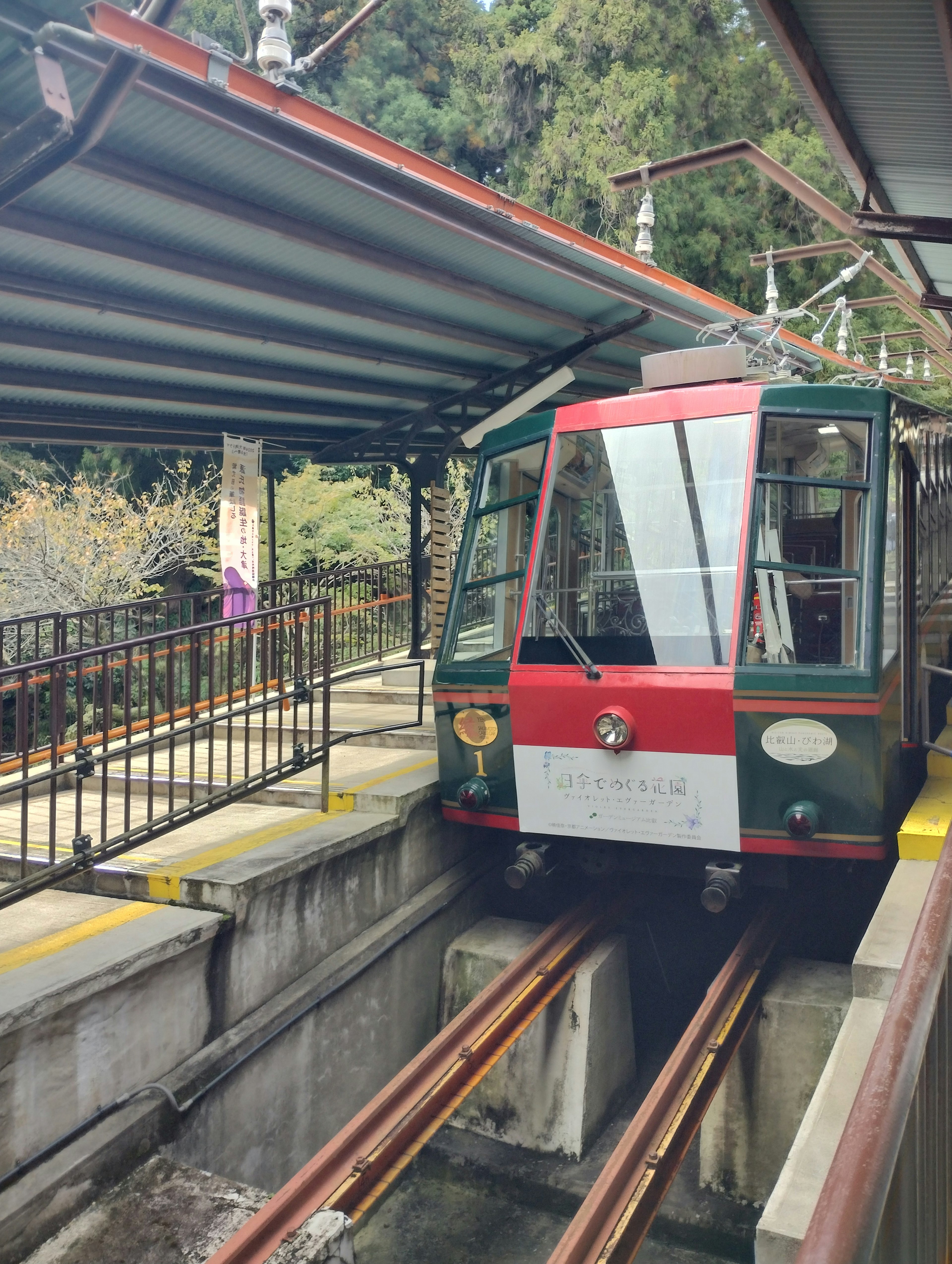 A red and green cable car stopped at a station