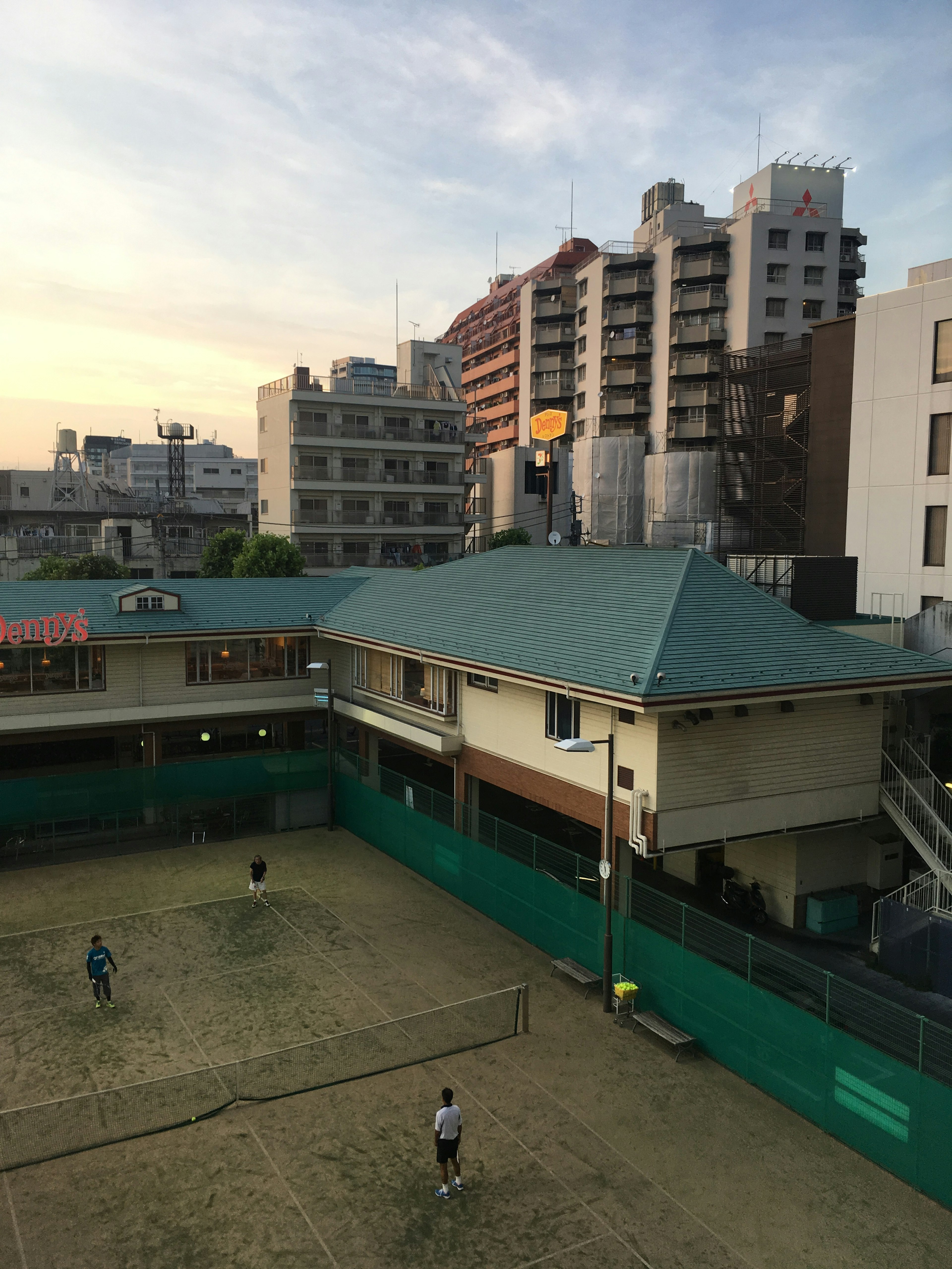 Des personnes jouant au tennis au coucher du soleil avec des bâtiments en arrière-plan