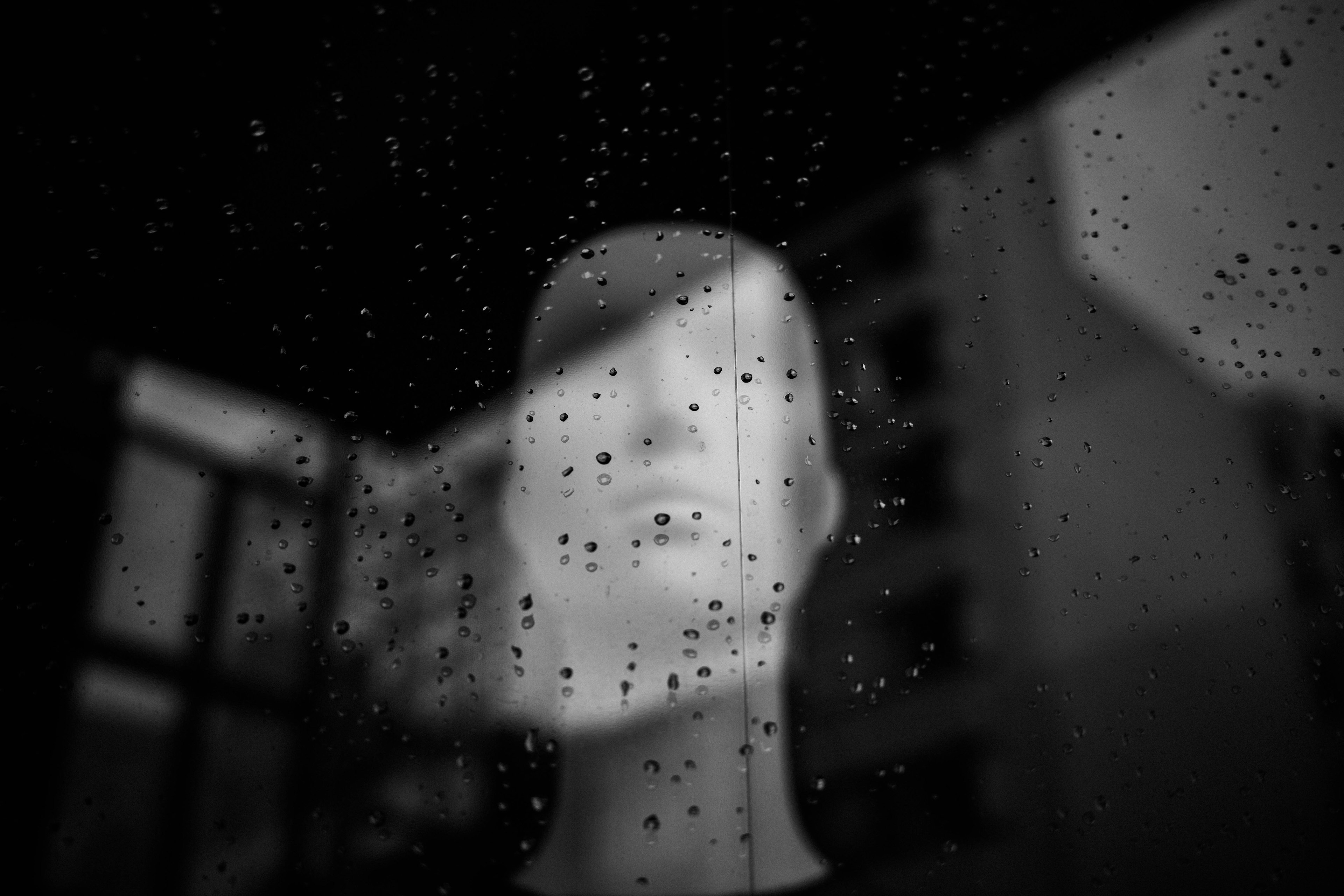 A white mannequin face visible through a rain-soaked window