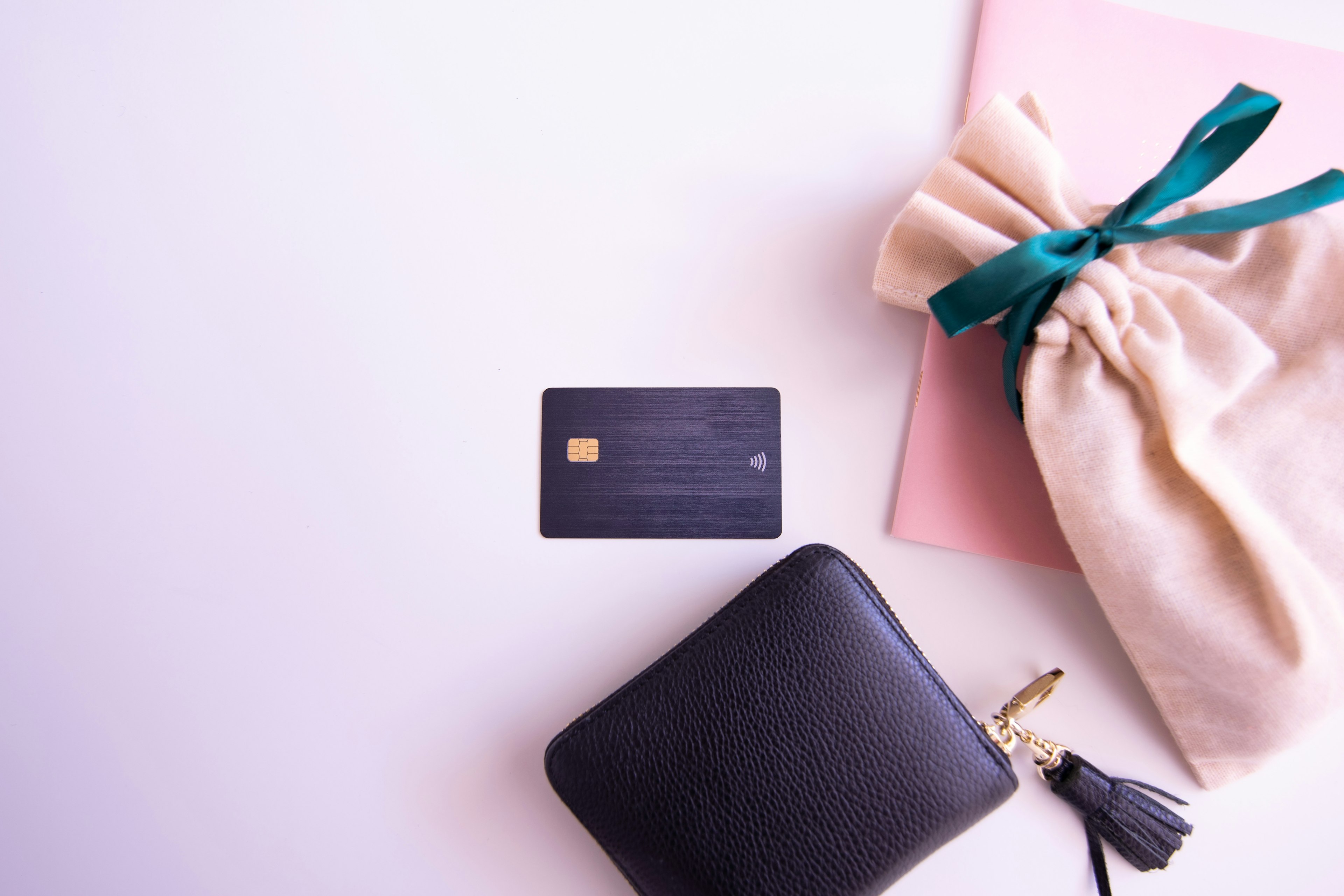 Black wallet with a credit card pink notebook and a cloth bag with a green ribbon