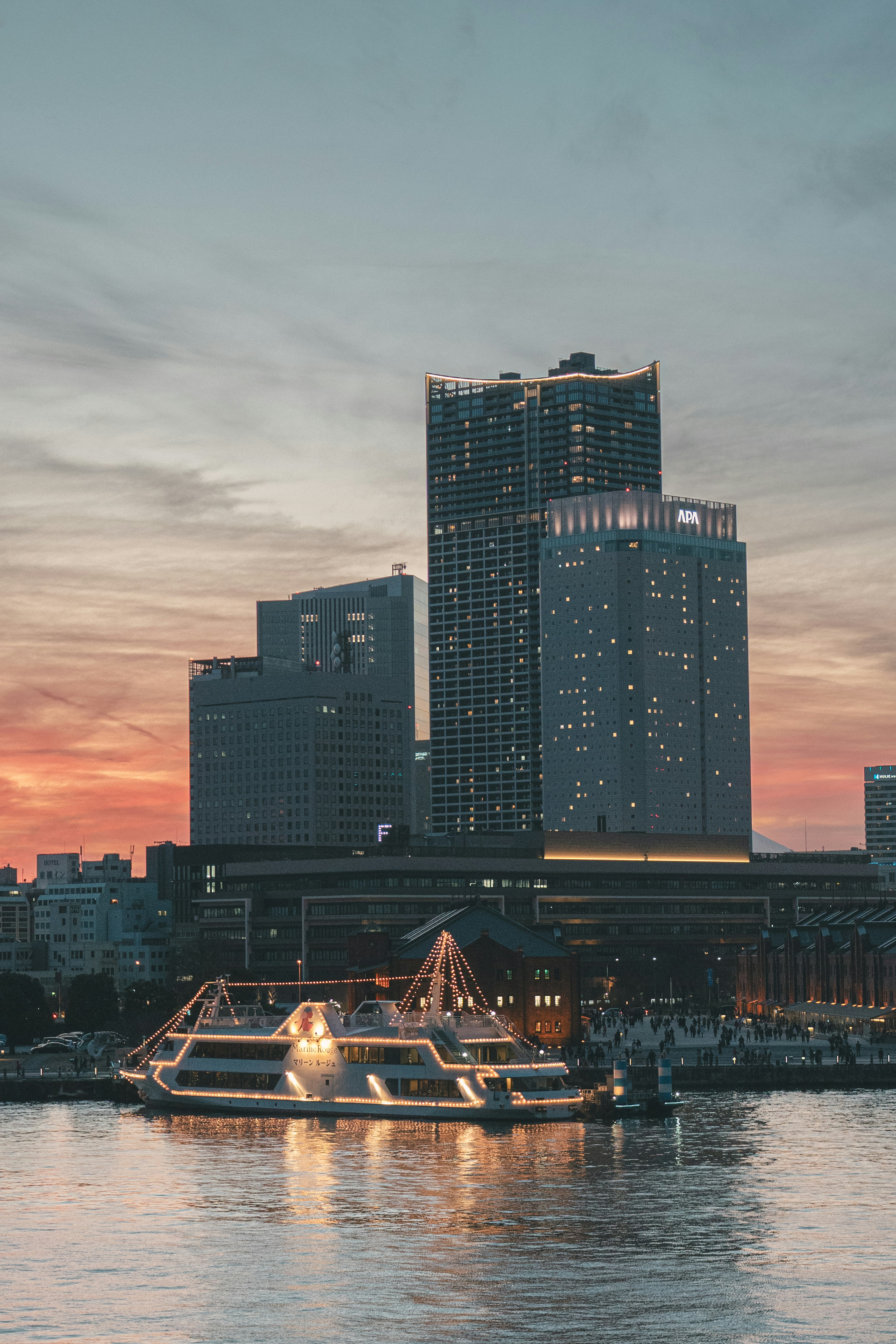 夕焼けの空の下にそびえる高層ビルと川に浮かぶ船