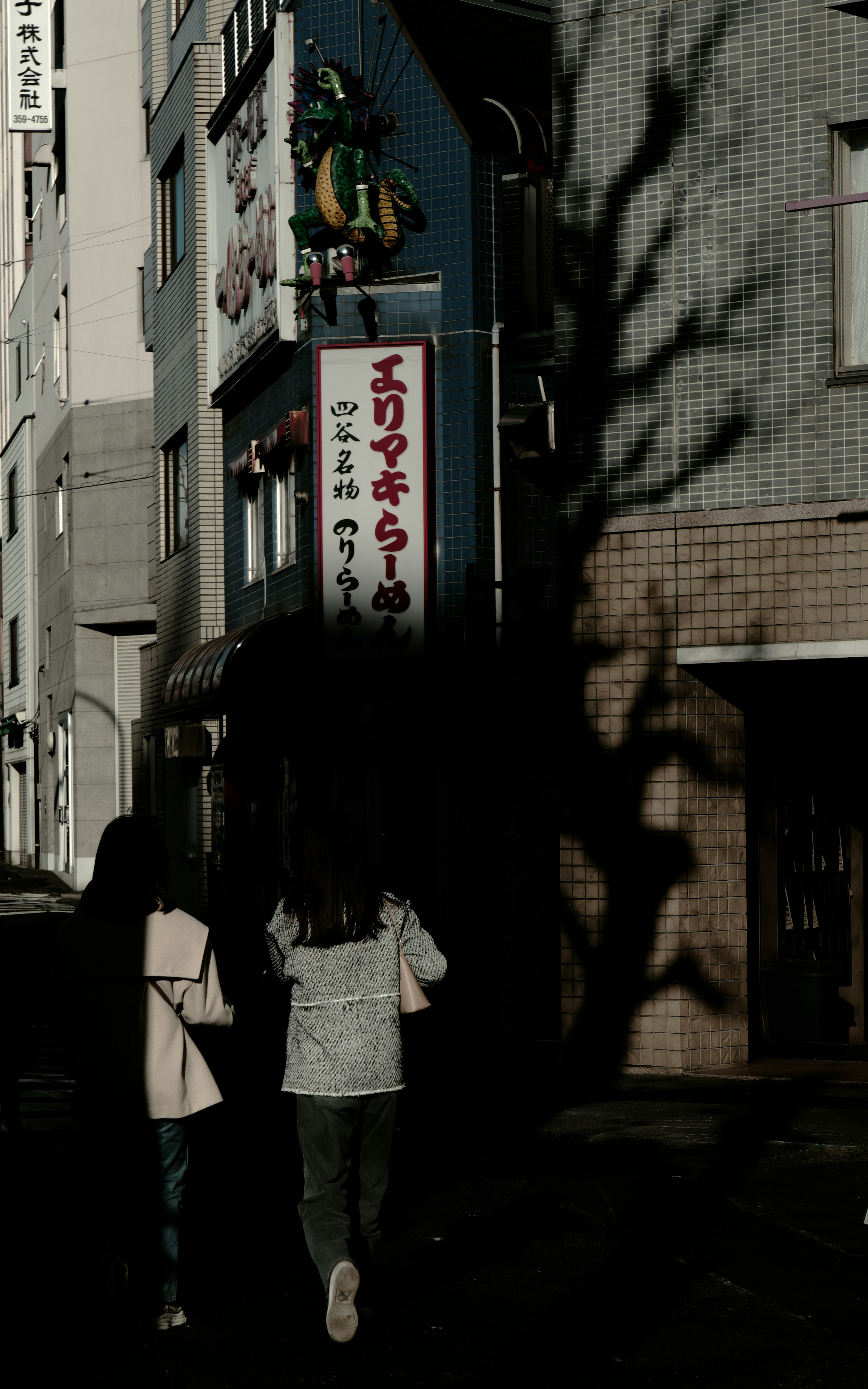 Dos mujeres caminando por una calle débilmente iluminada con sombras de edificios