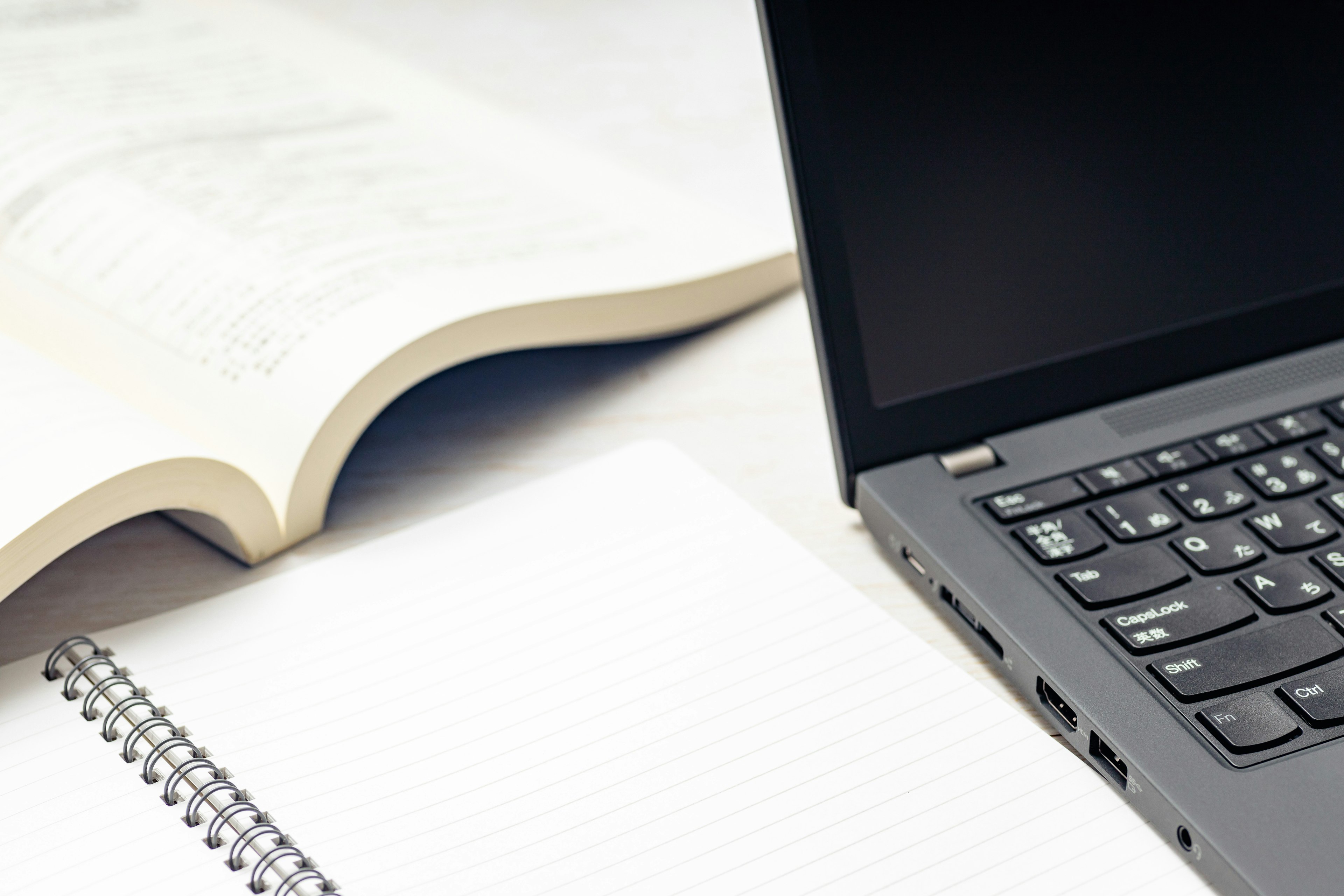 Image d'un ordinateur portable à côté d'un manuel ouvert avec un cahier vierge et un clavier noir visible