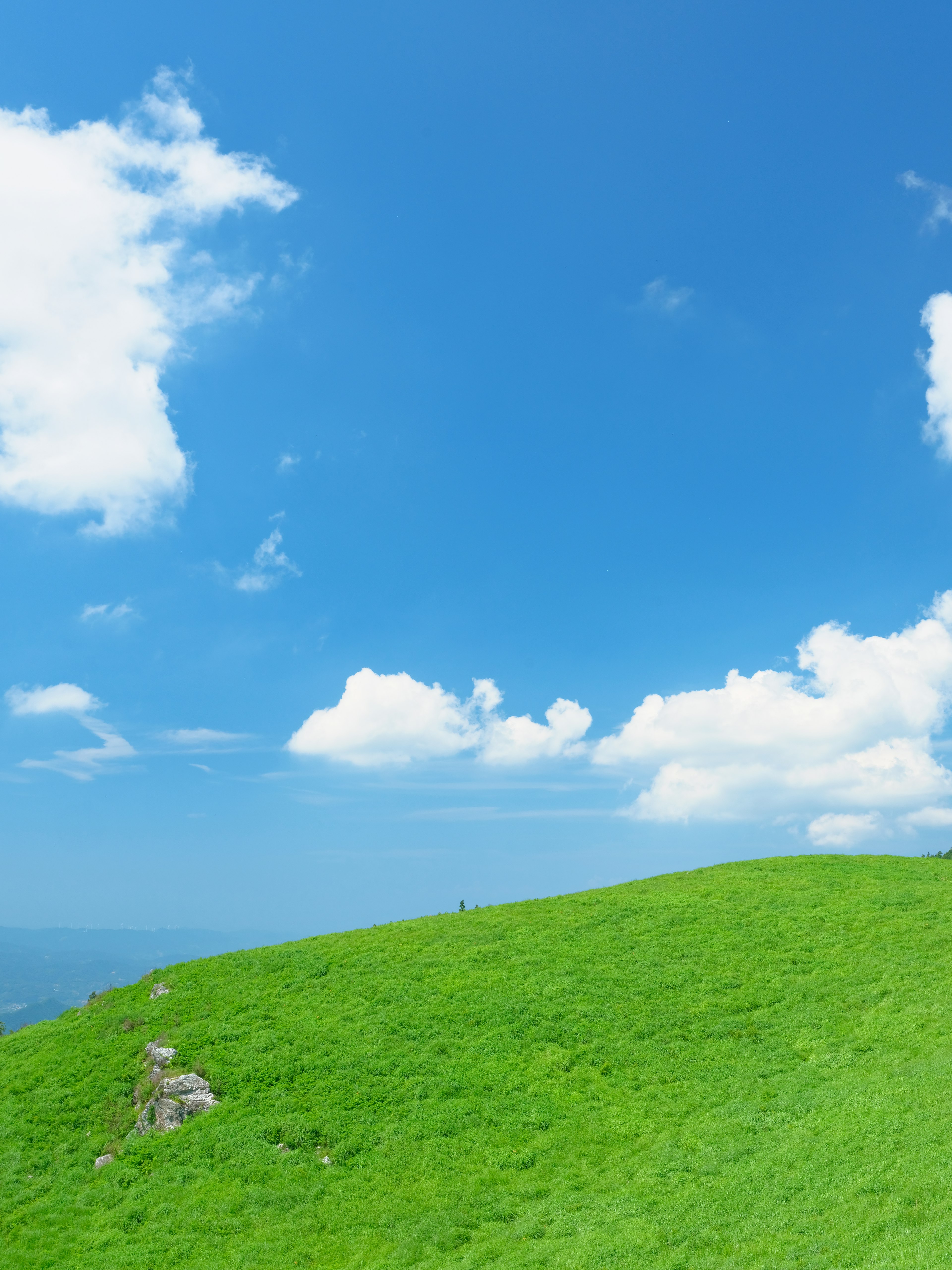 Vibrant green hill under a clear blue sky with fluffy white clouds