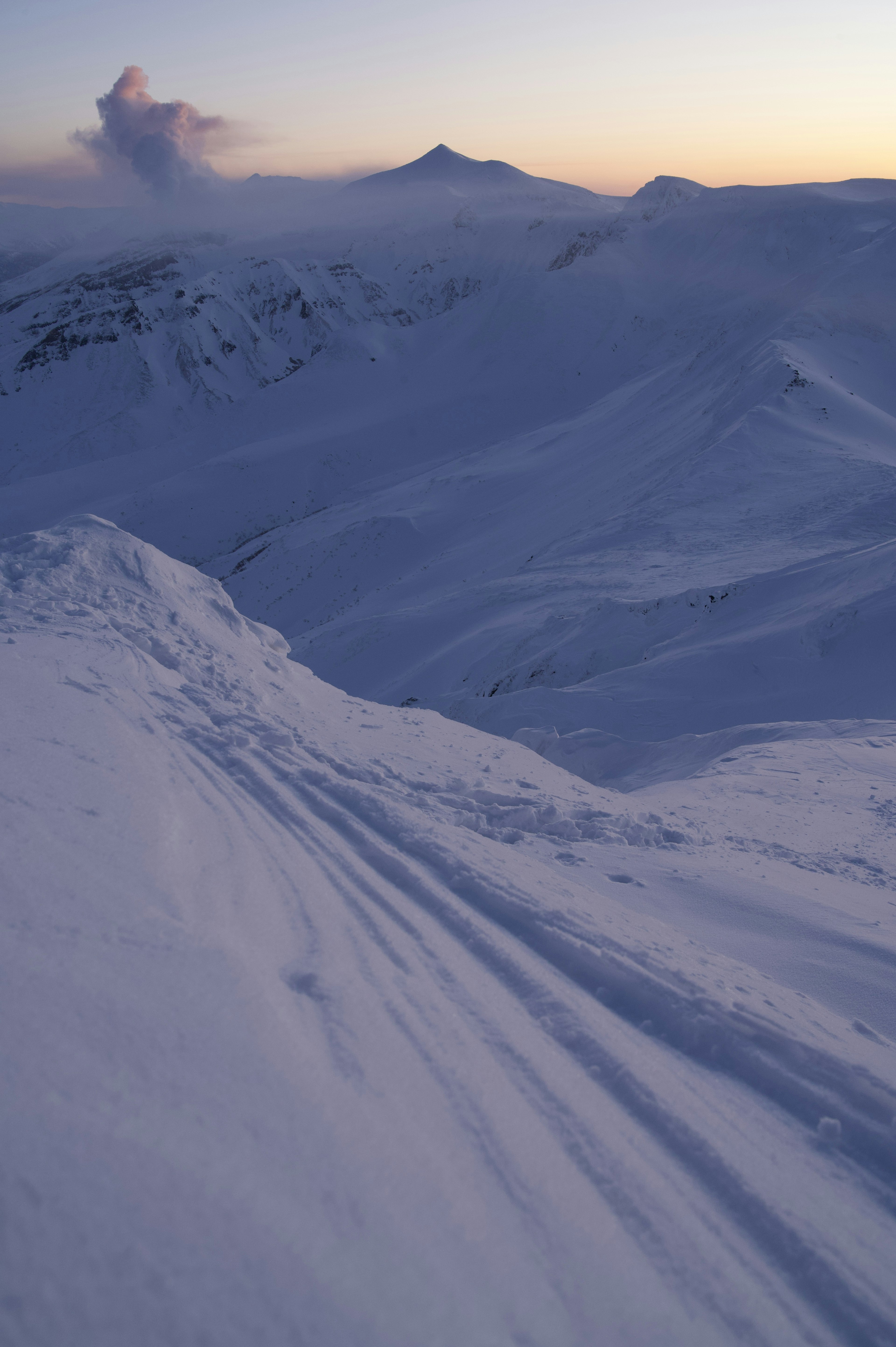 Snow-covered mountain landscape with ski tracks and sunset sky