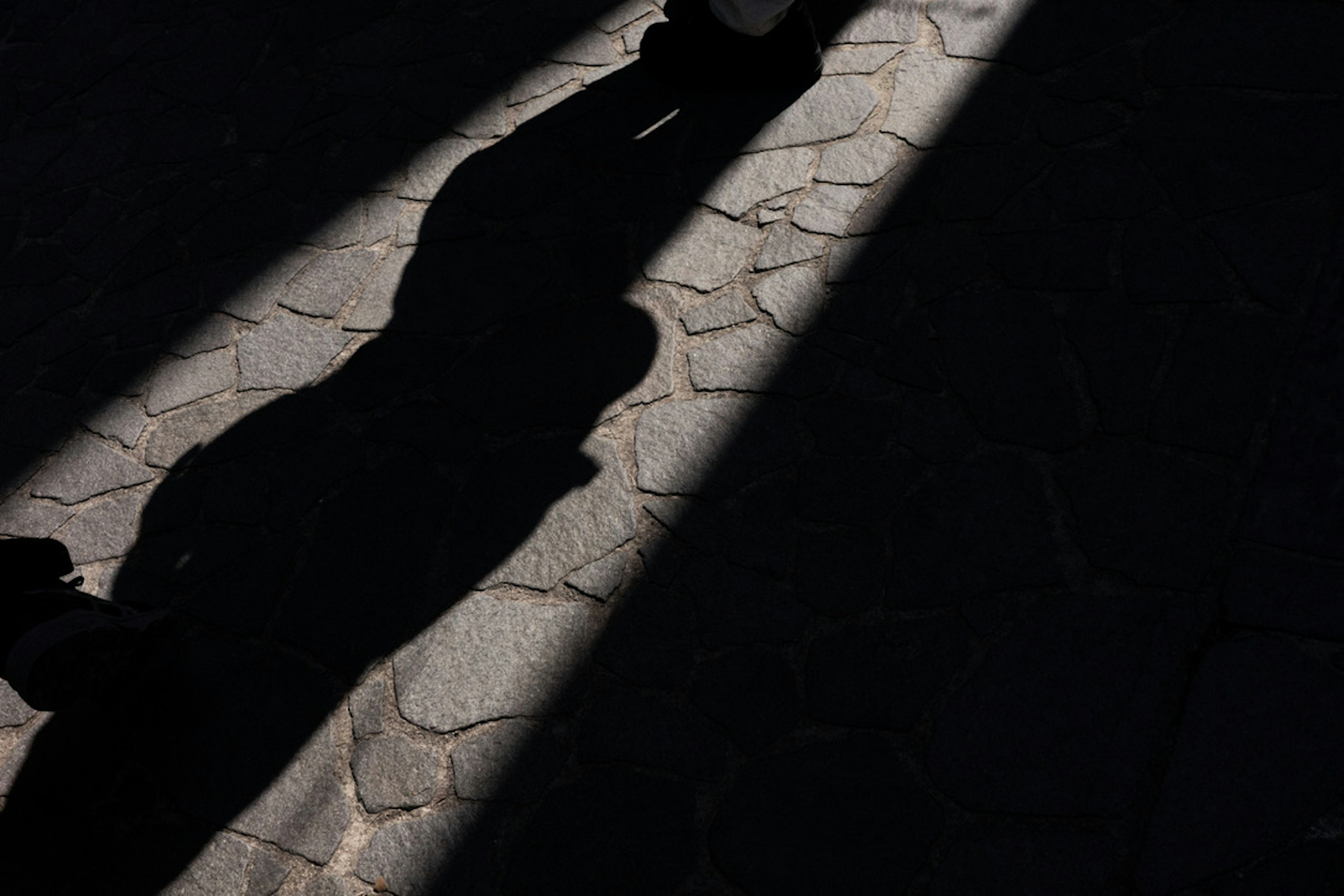 Schatten auf einem mit Steinen gepflasterten Weg, beleuchtet von Lichtstrahlen