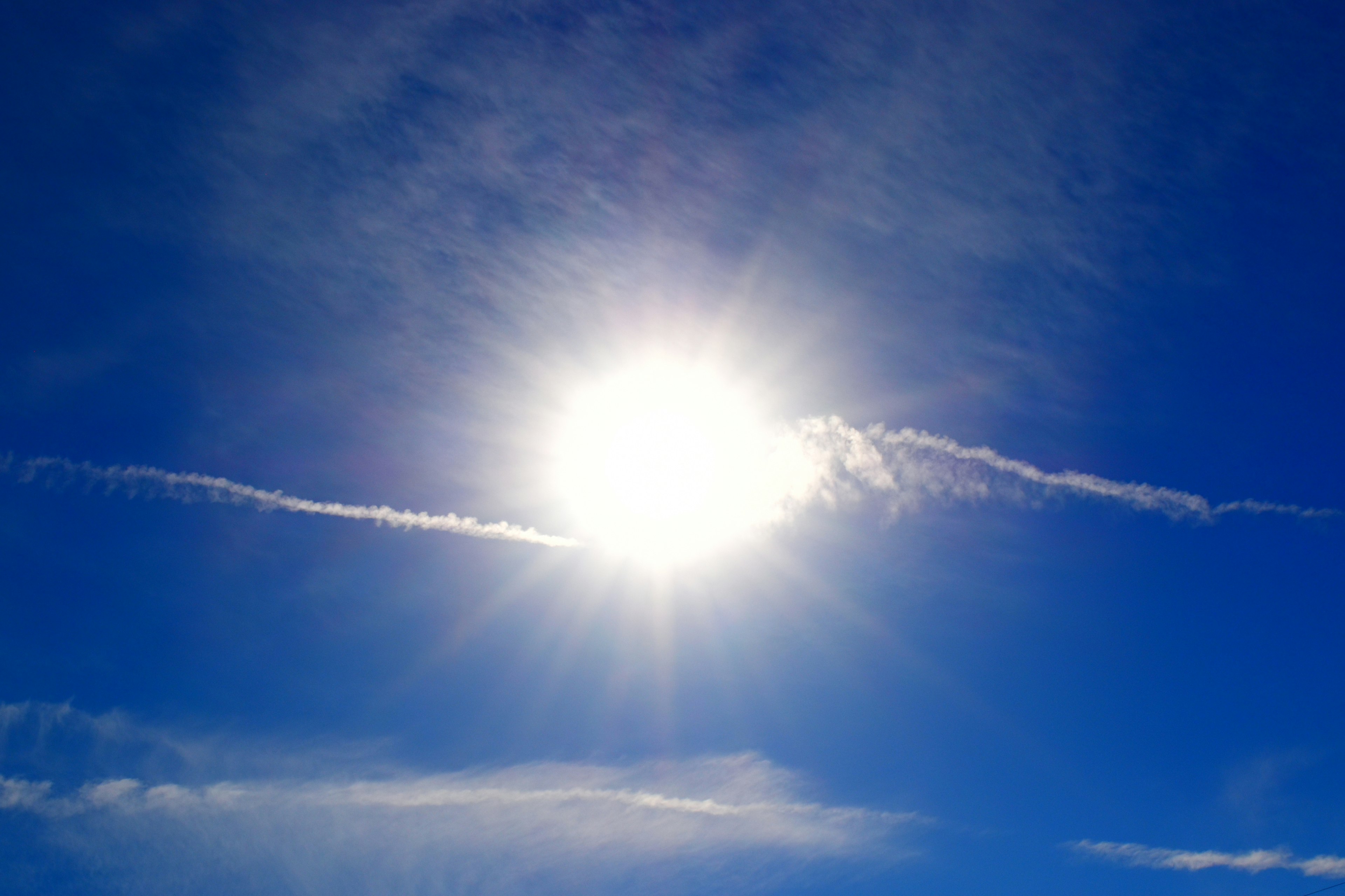 Sol brillante en un cielo azul con estelas de nubes blancas