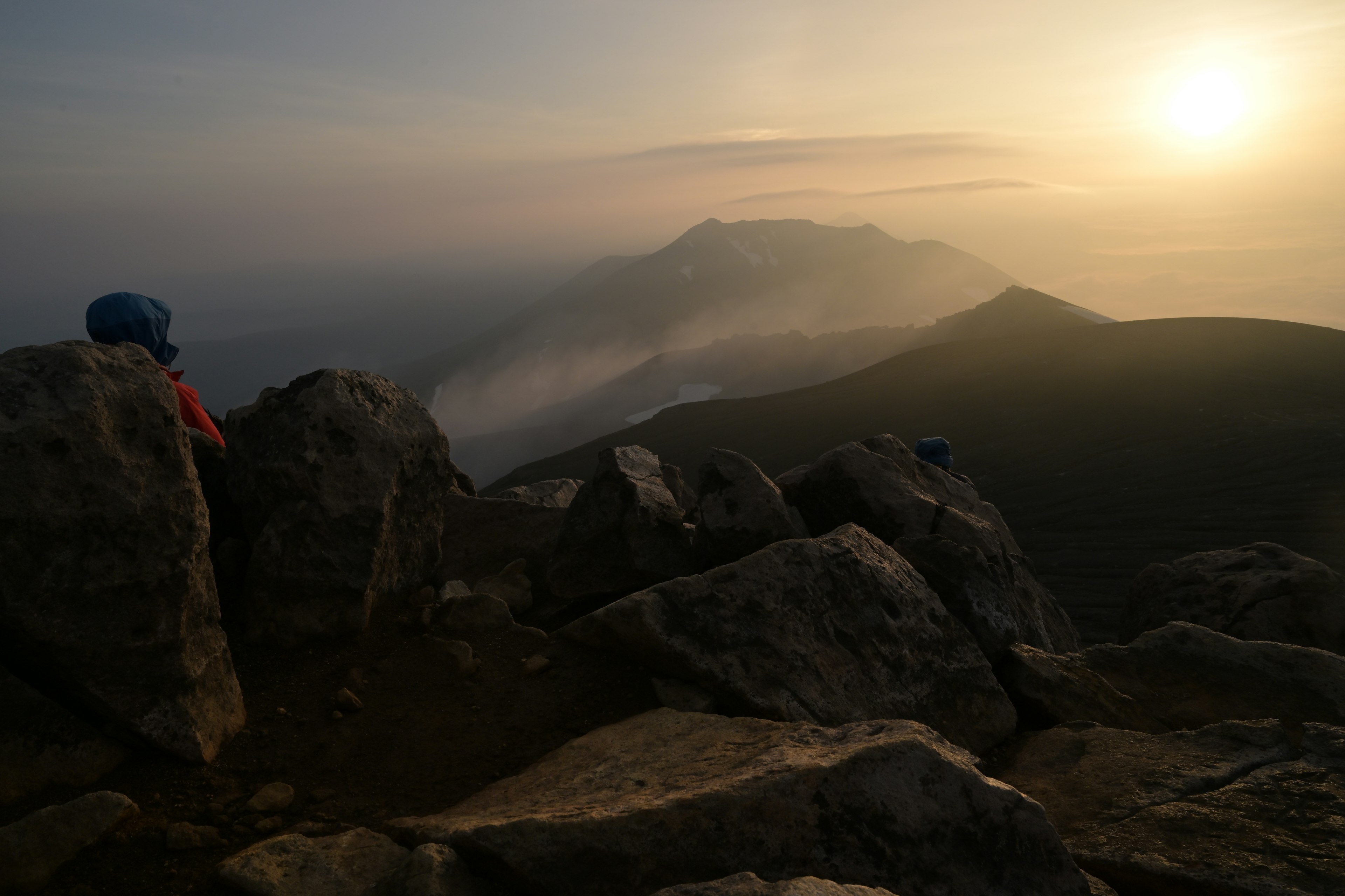 Pemandangan matahari terbit yang indah dari puncak gunung dengan latar depan berbatu dan perbukitan berkabut