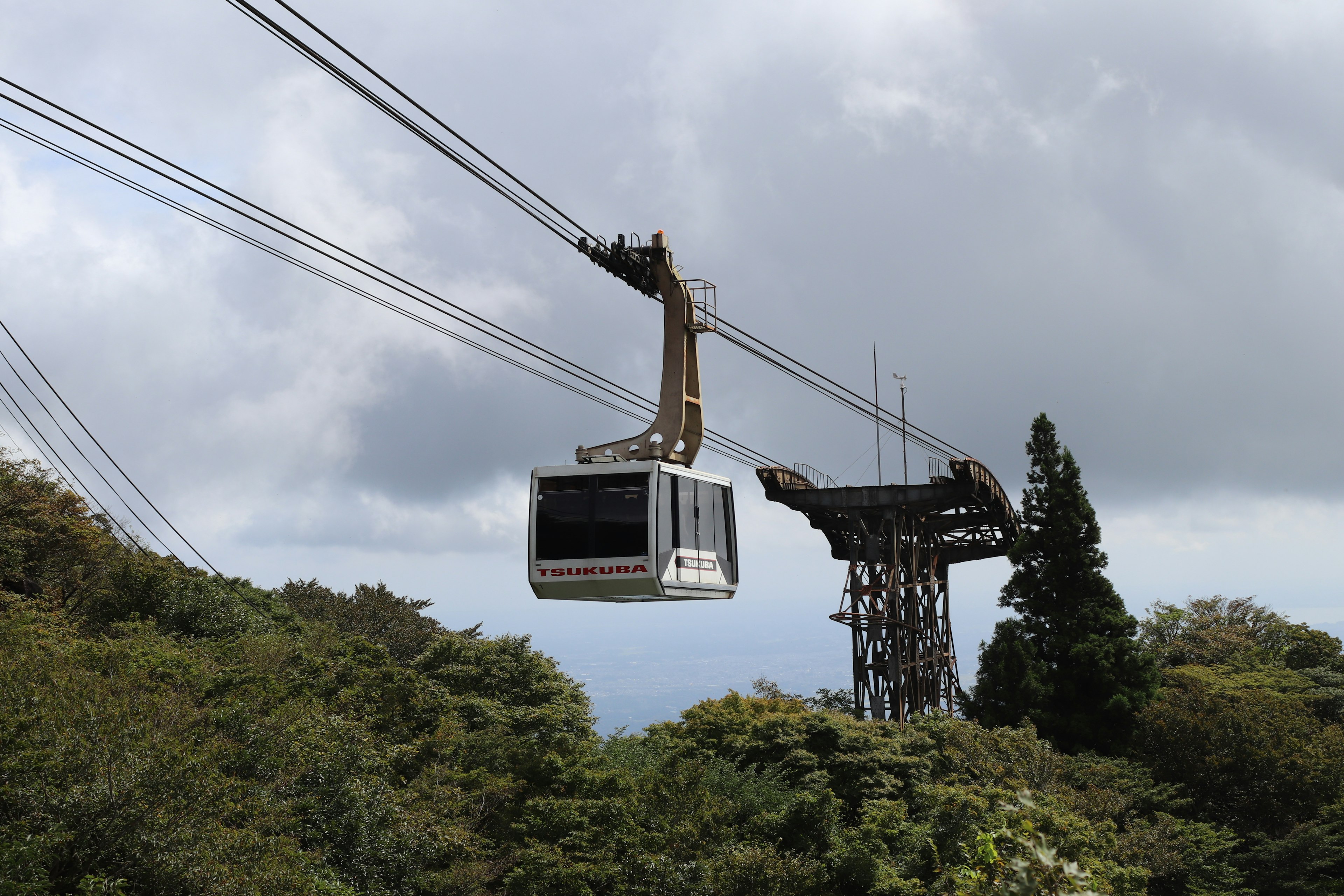 A cable car gondola moving above lush green trees