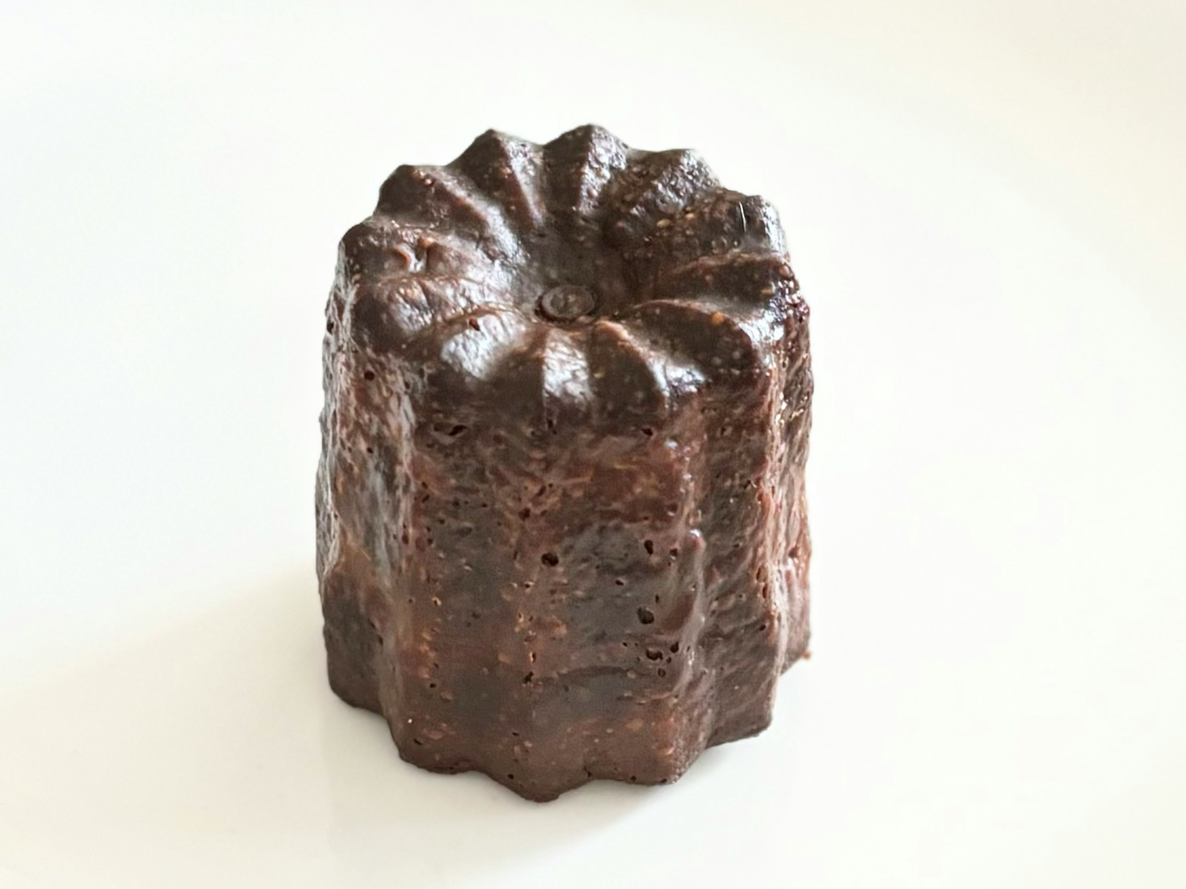 A chocolate-colored canelé placed on a white background