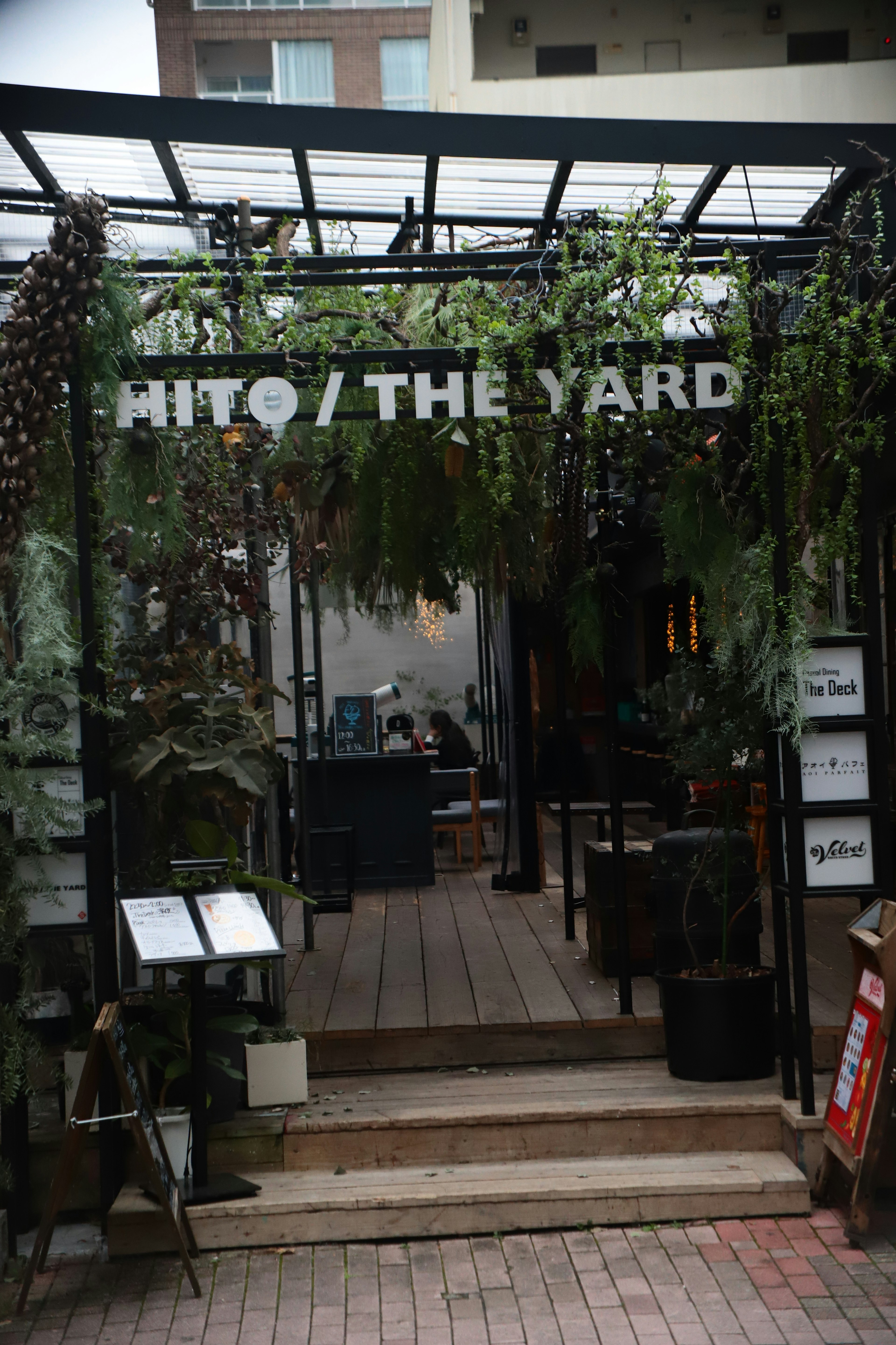 緑に囲まれたカフェの入り口で、HITO / THE YARDの看板が見える