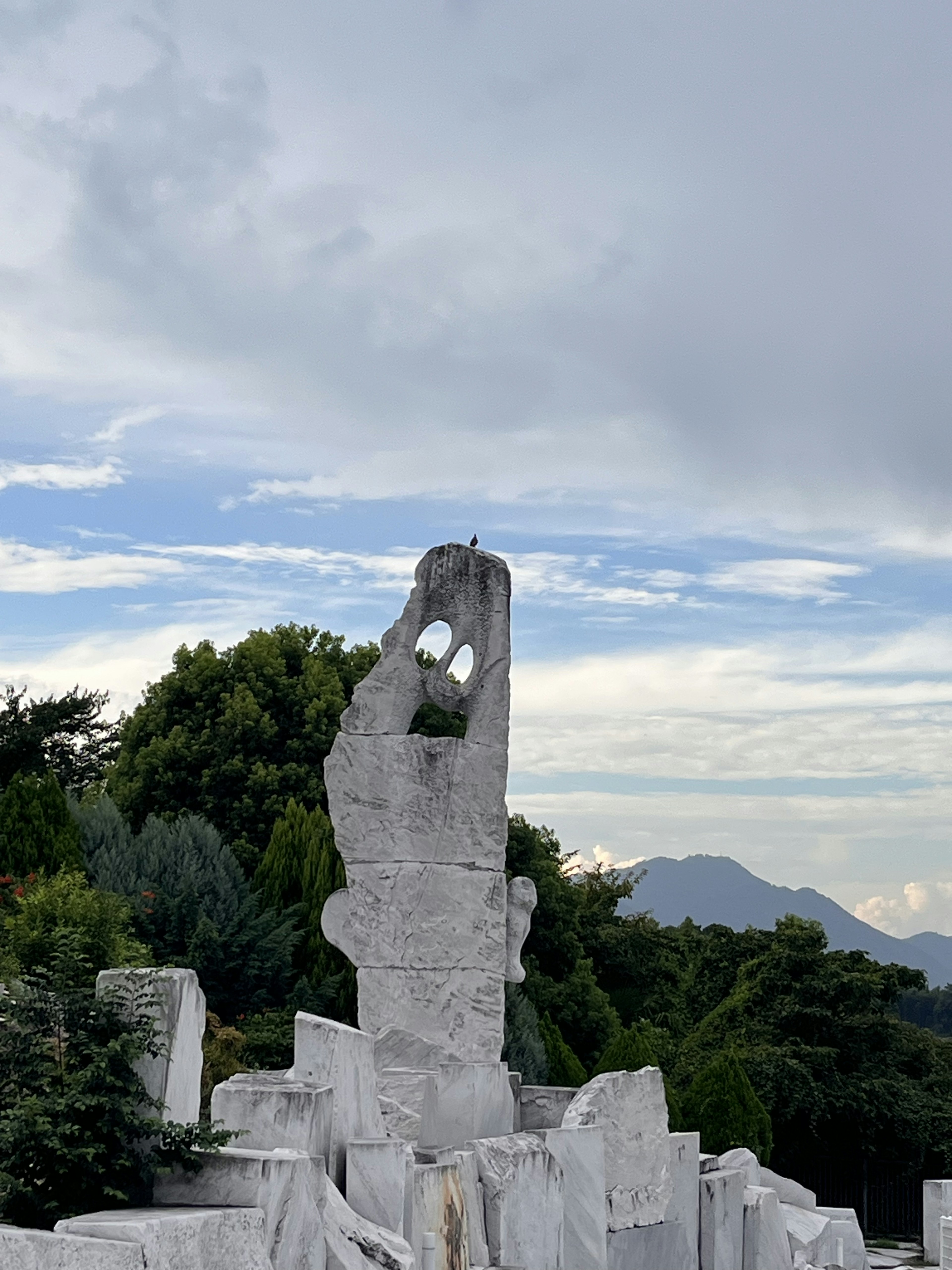 白い石の彫刻が青い空と緑の木々の背景に立っている