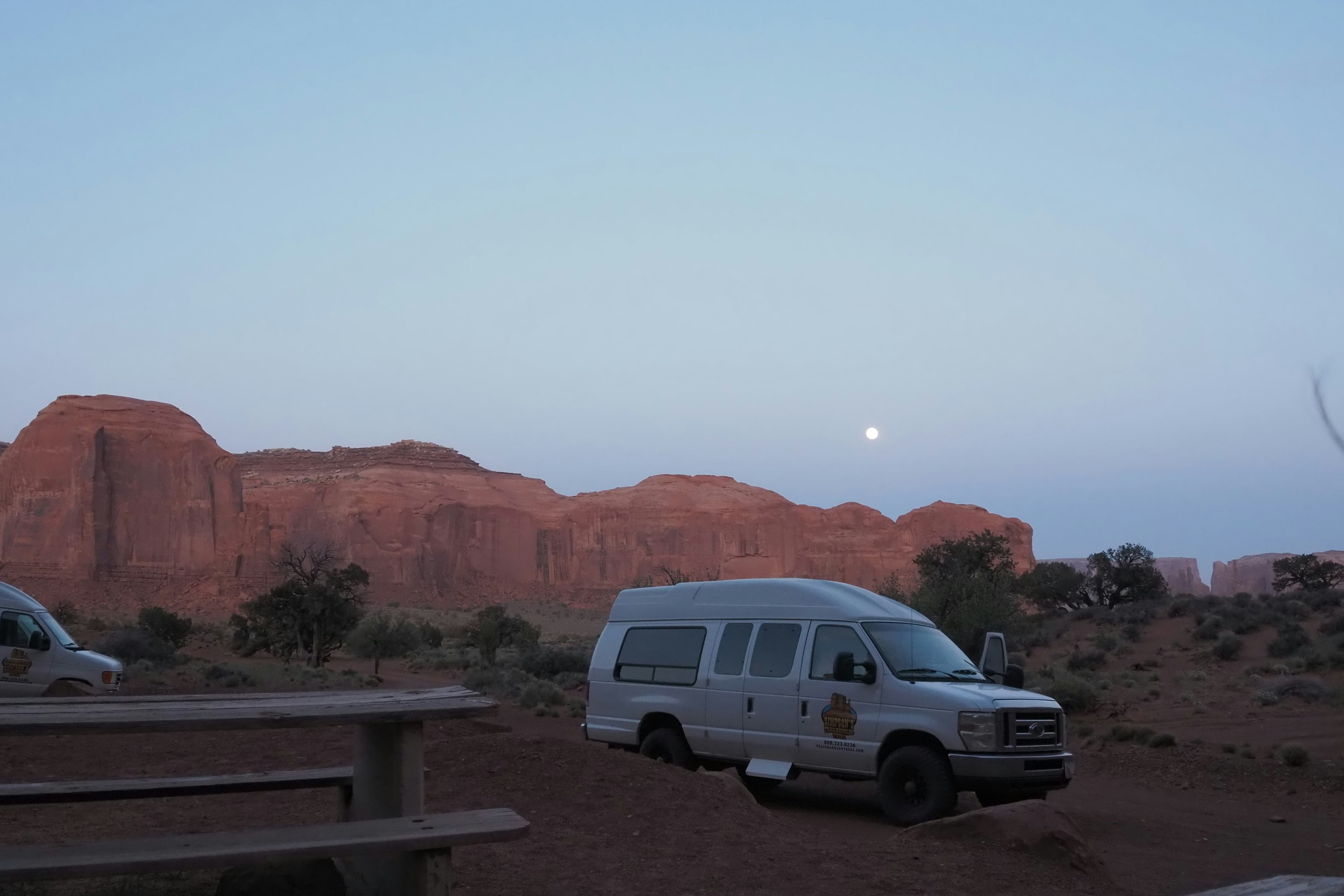 Fourgon blanc garé dans la Vallée des Monuments au crépuscule avec la lune en arrière-plan