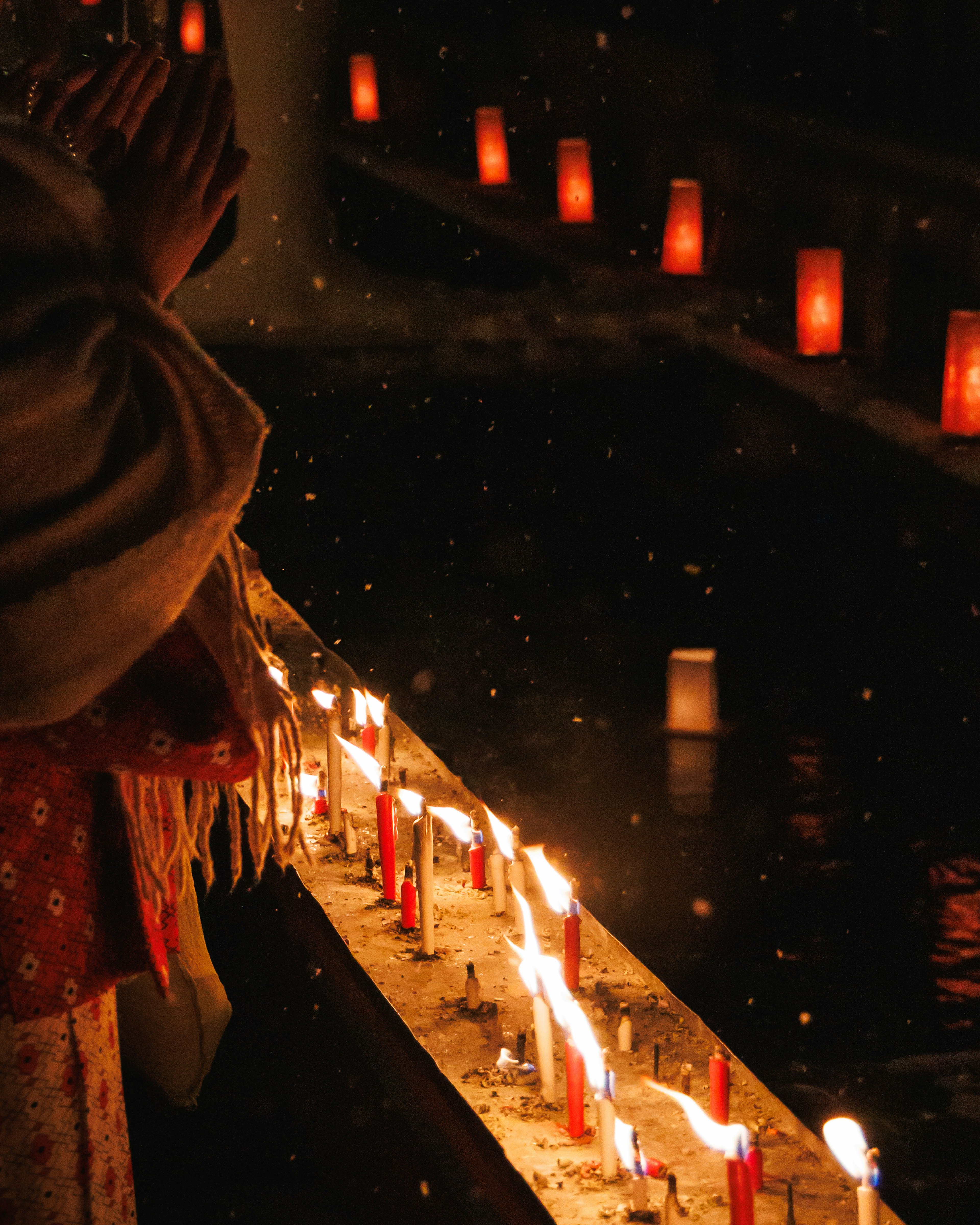 A person praying with glowing lanterns and candles reflecting in the water at night